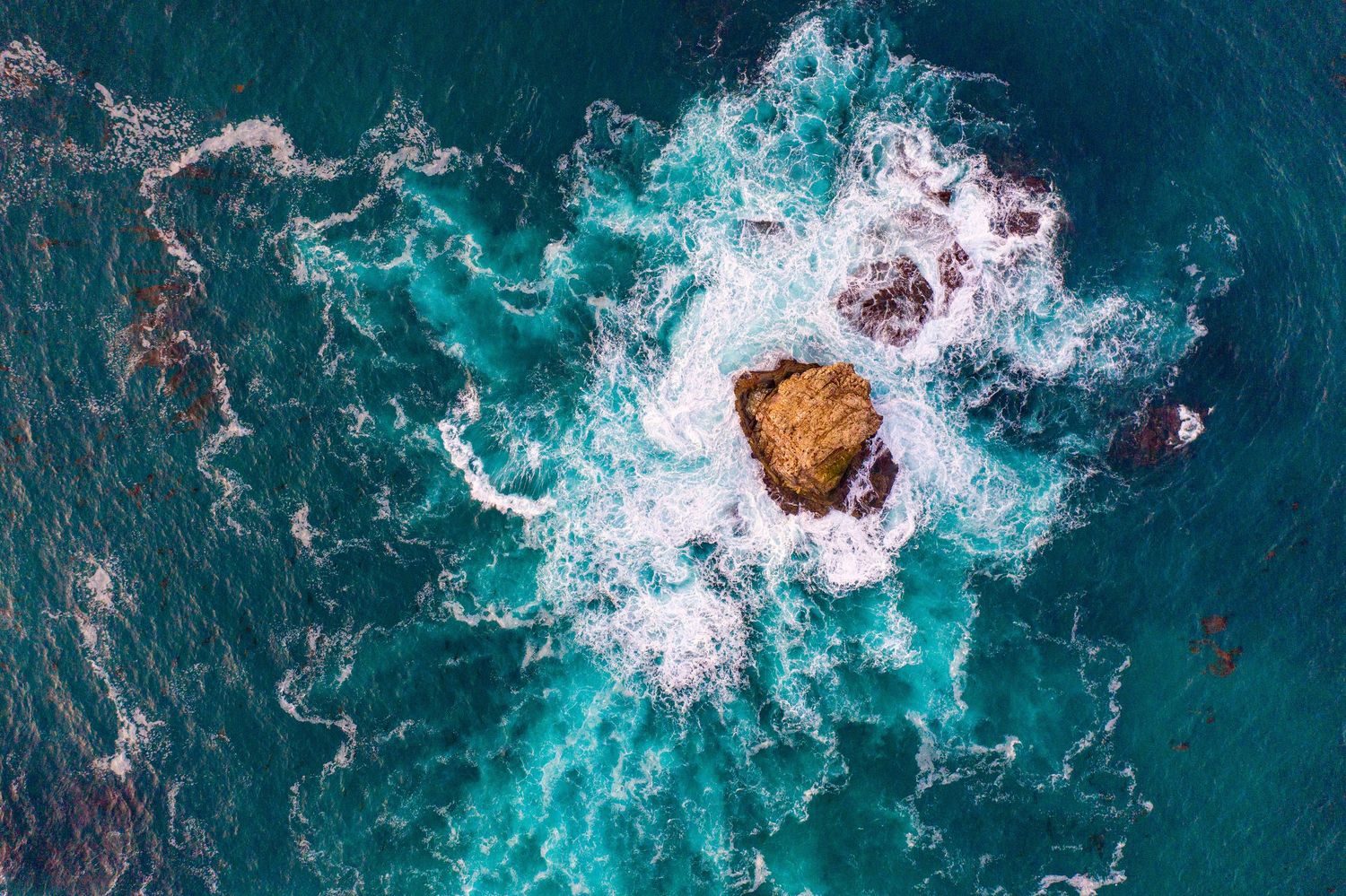Aerial view of turquoise ocean waves crashing against rocky coastline creating white foam patterns.