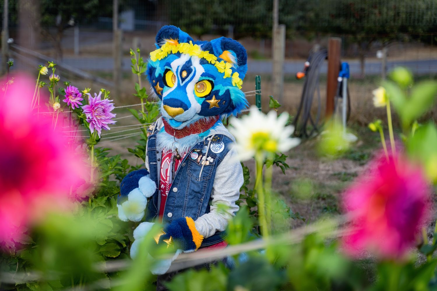Bright fursuit characters pose among pink and white flowers in a garden setting.