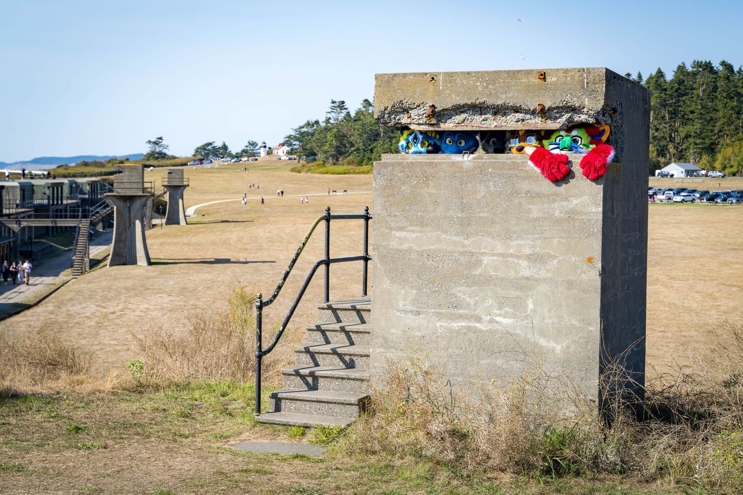 Group walking on path beside concrete military fortification under blue sky.
