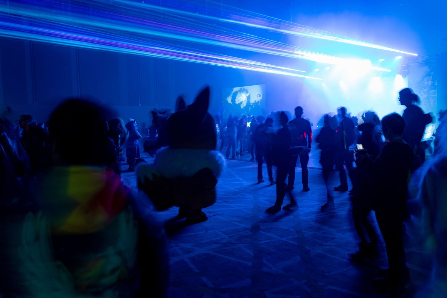 People dancing in a dark nightclub with blue lighting and fog effects creating an atmospheric party environment.