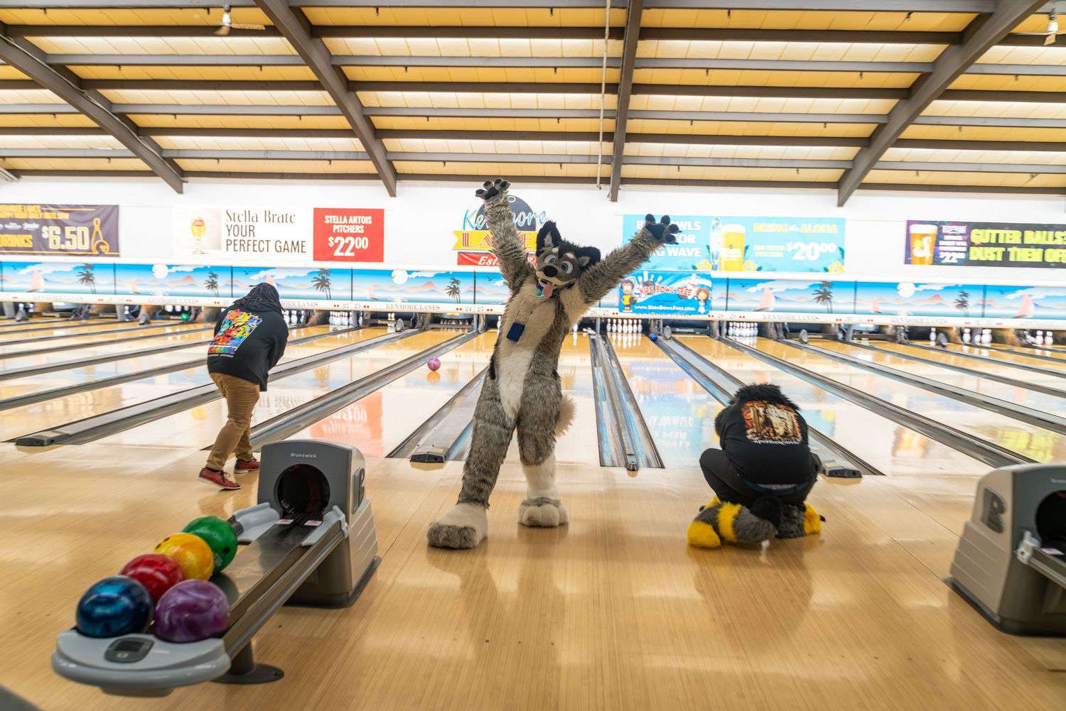 A fursuited character strikes a celebratory pose between bowling lanes.