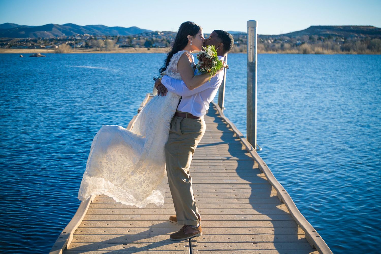 Wedding couple sharing romantic moments on a wooden dock by a scenic lake.