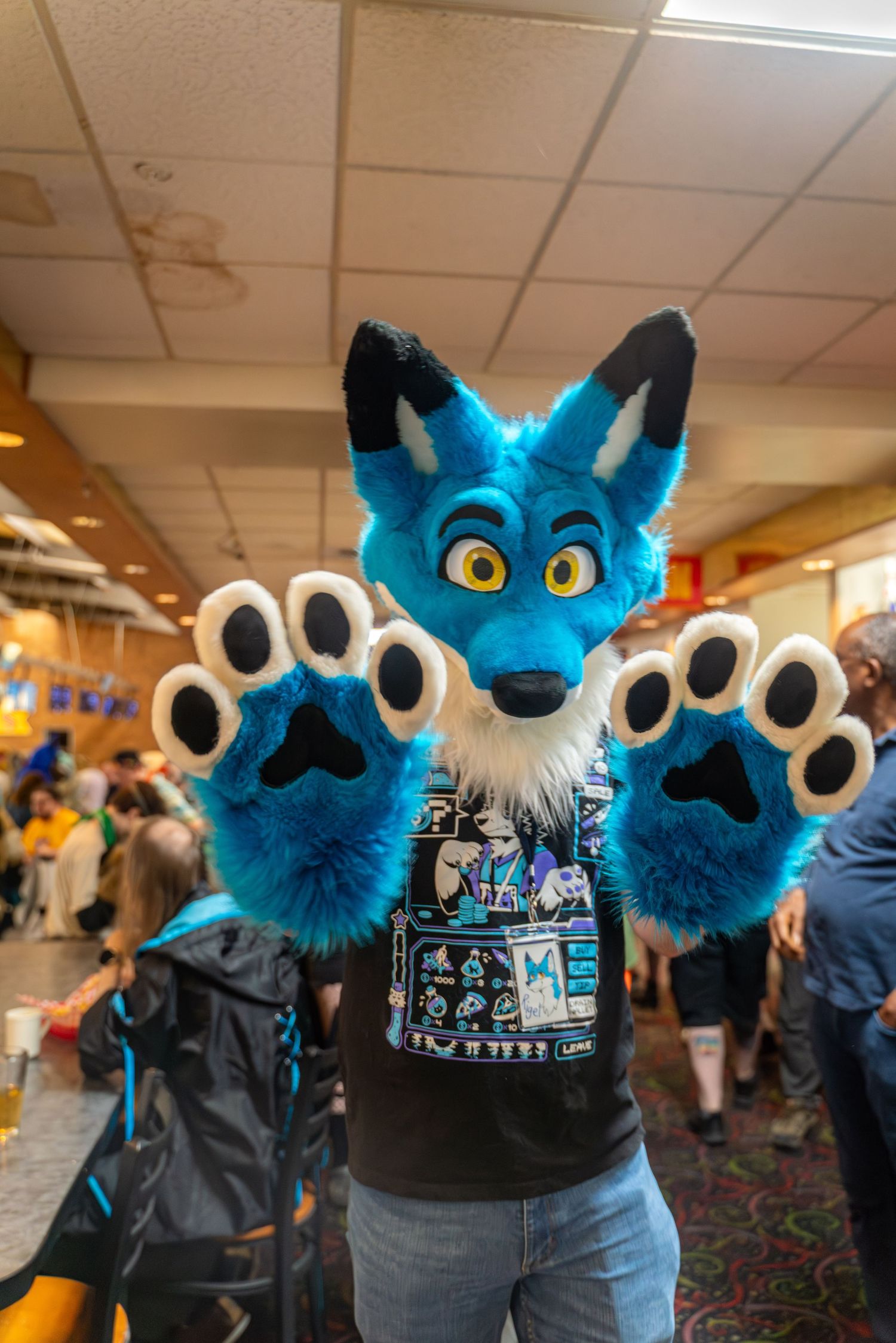Multiple blue fursuit characters with large eyes stand together wearing matching black t-shirts.