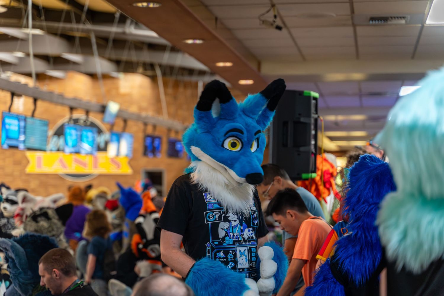 Costumed characters in bright blue fur gather at a crowded indoor convention space.