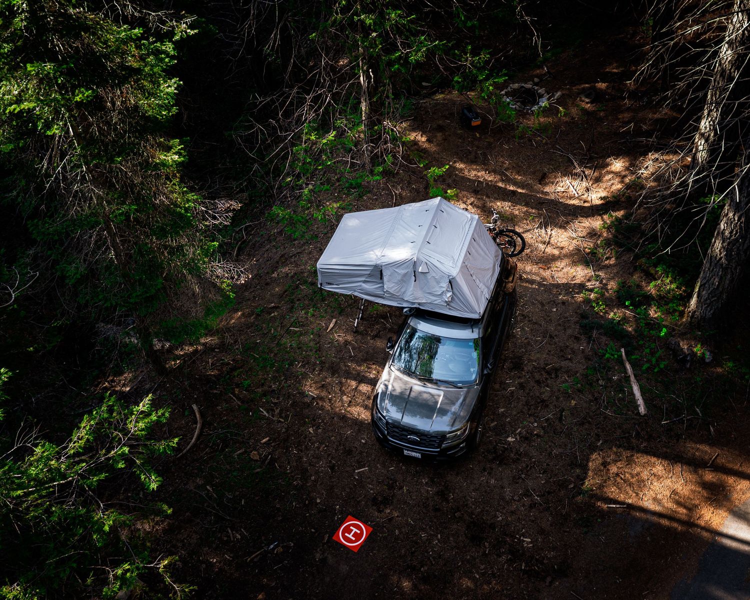 Aerial view of cars parked along a forest trail surrounded by tall trees.