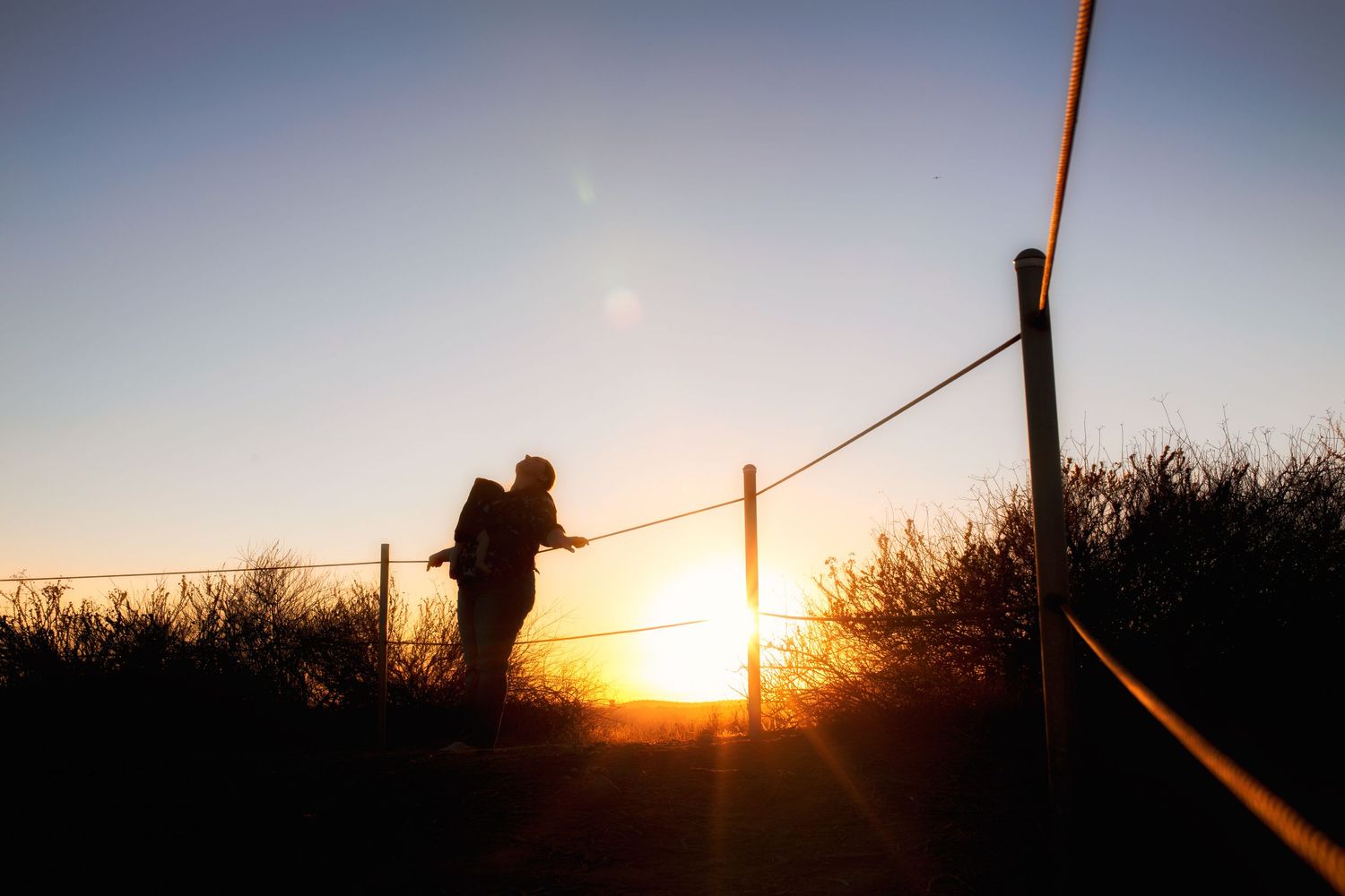 Silhouetted fence posts against dramatic orange sunset sky.