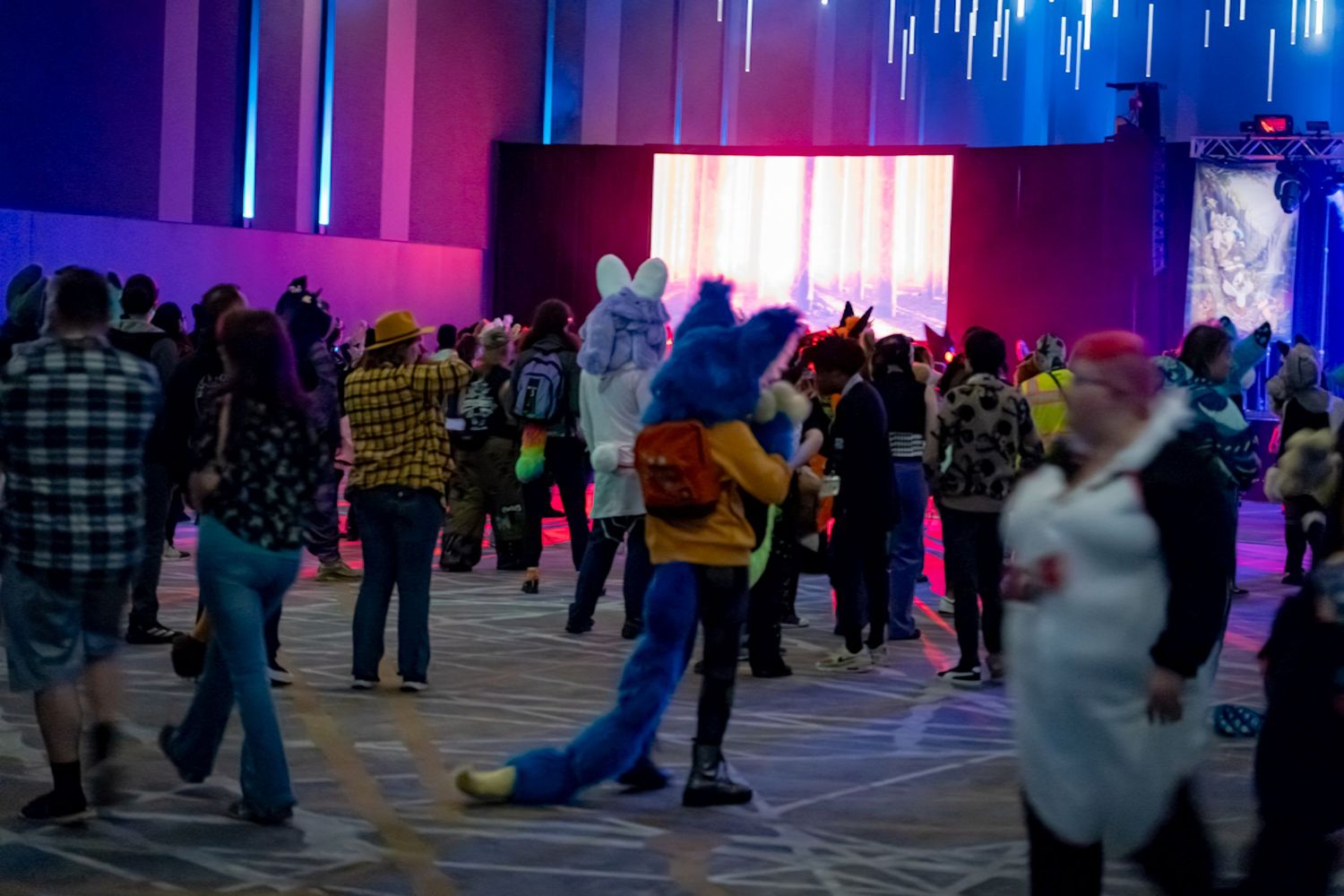 People dancing and socializing at a nightclub with colorful pink and blue lighting effects.