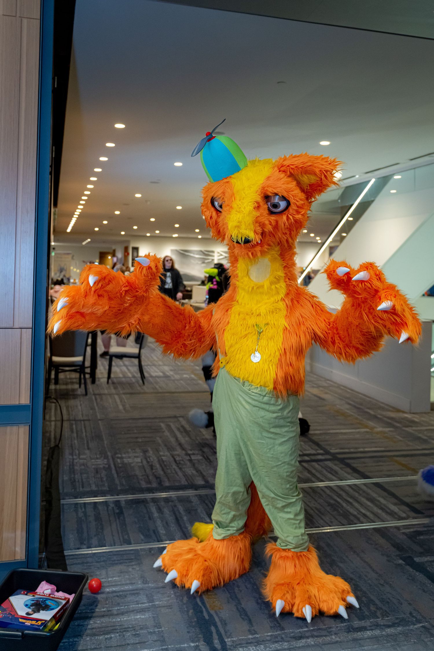 A bright orange and yellow furry mascot costume dancing in a carpeted conference room with mirrored walls.
