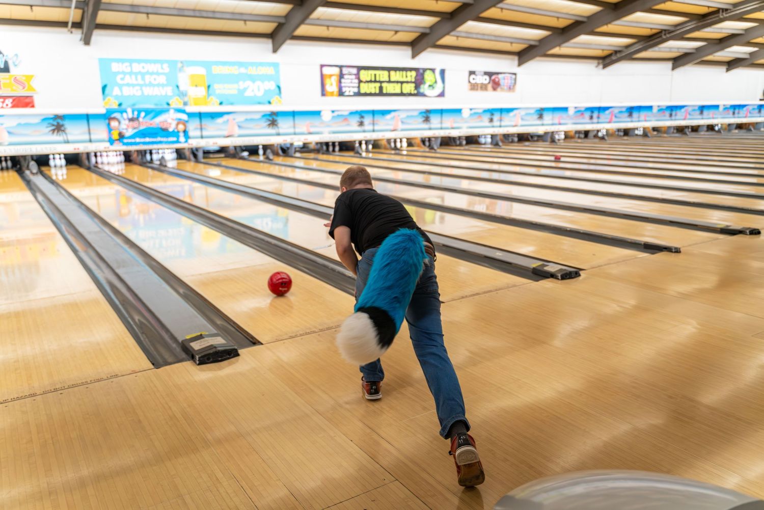 Several people bowling in costume at a brightly lit bowling center.
