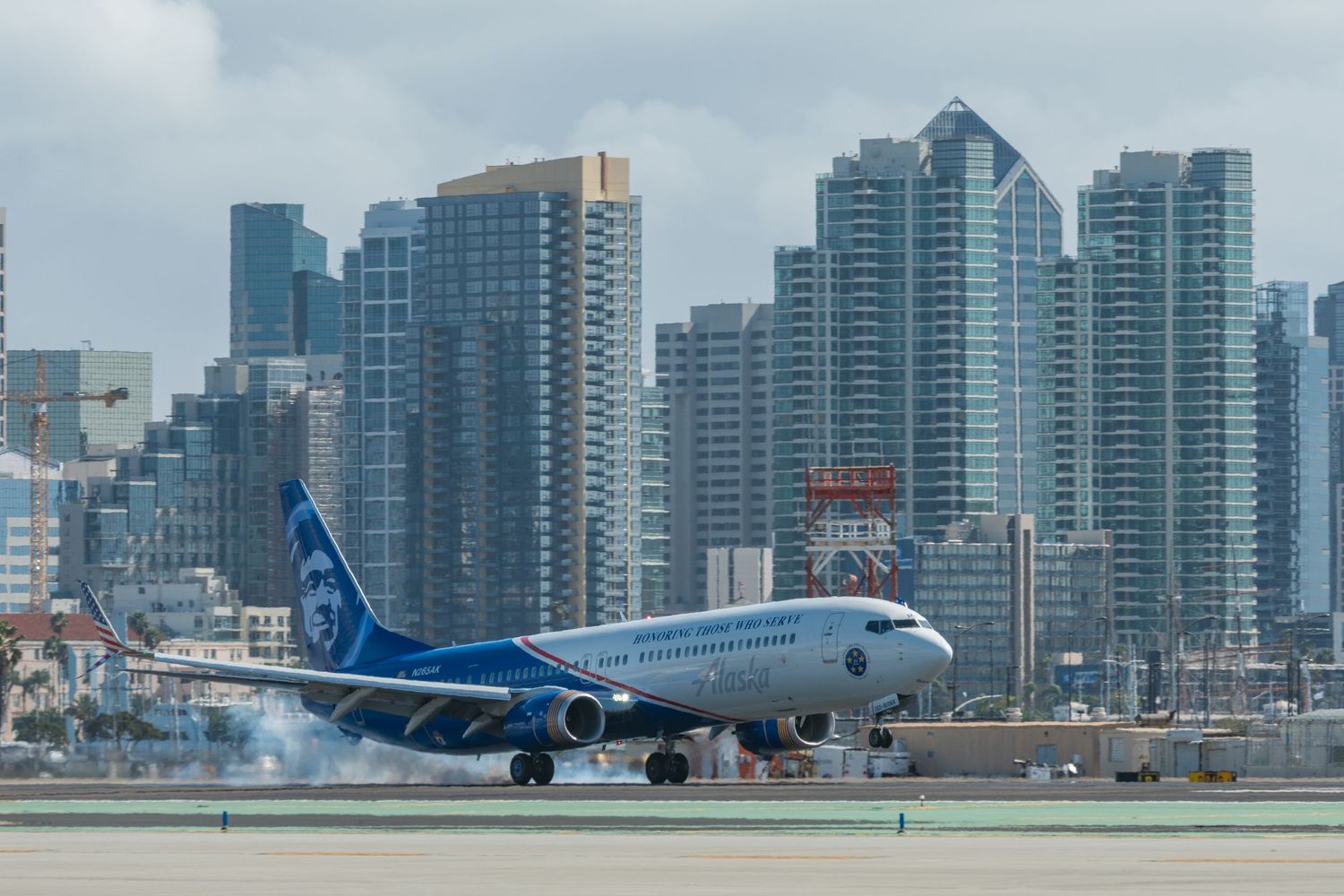 City skyline with modern skyscrapers visible behind a commercial aircraft at an airport.