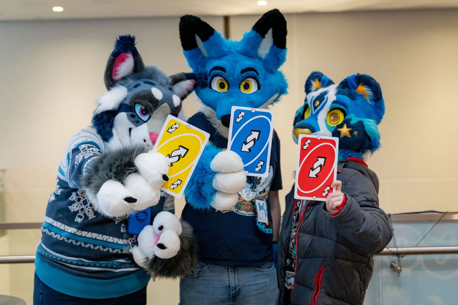 A group of fursuit characters gathered around a table playing Uno card game with colorful cards visible.