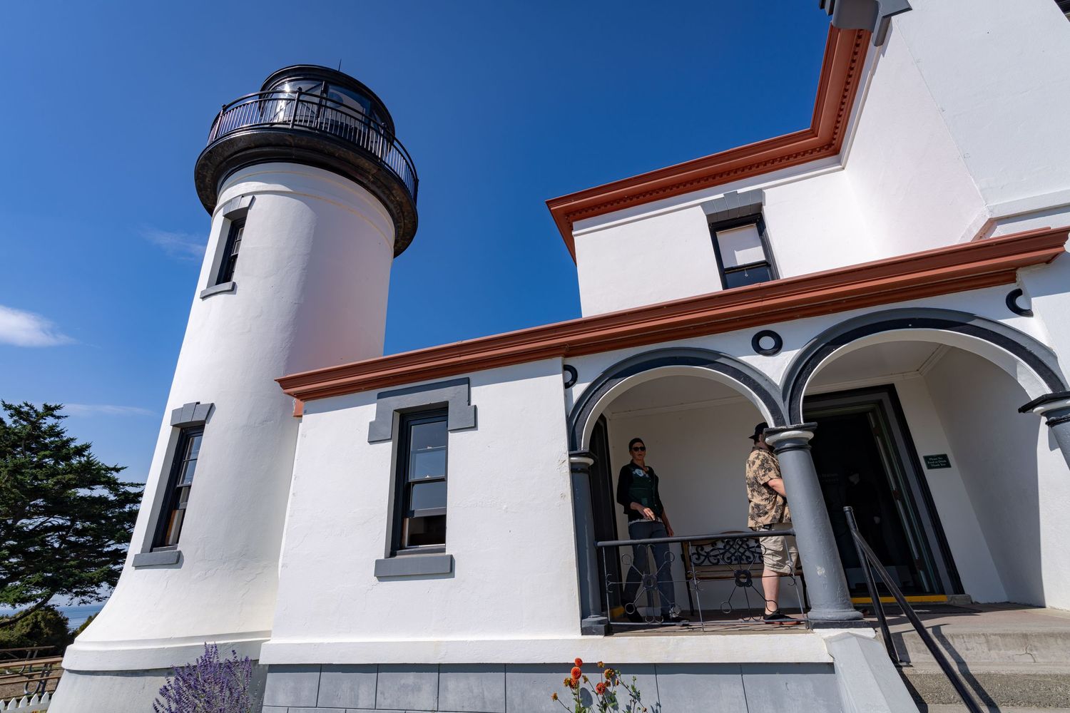 White lighthouse with red trim features a tall tower and covered porch with arched colonnade.
