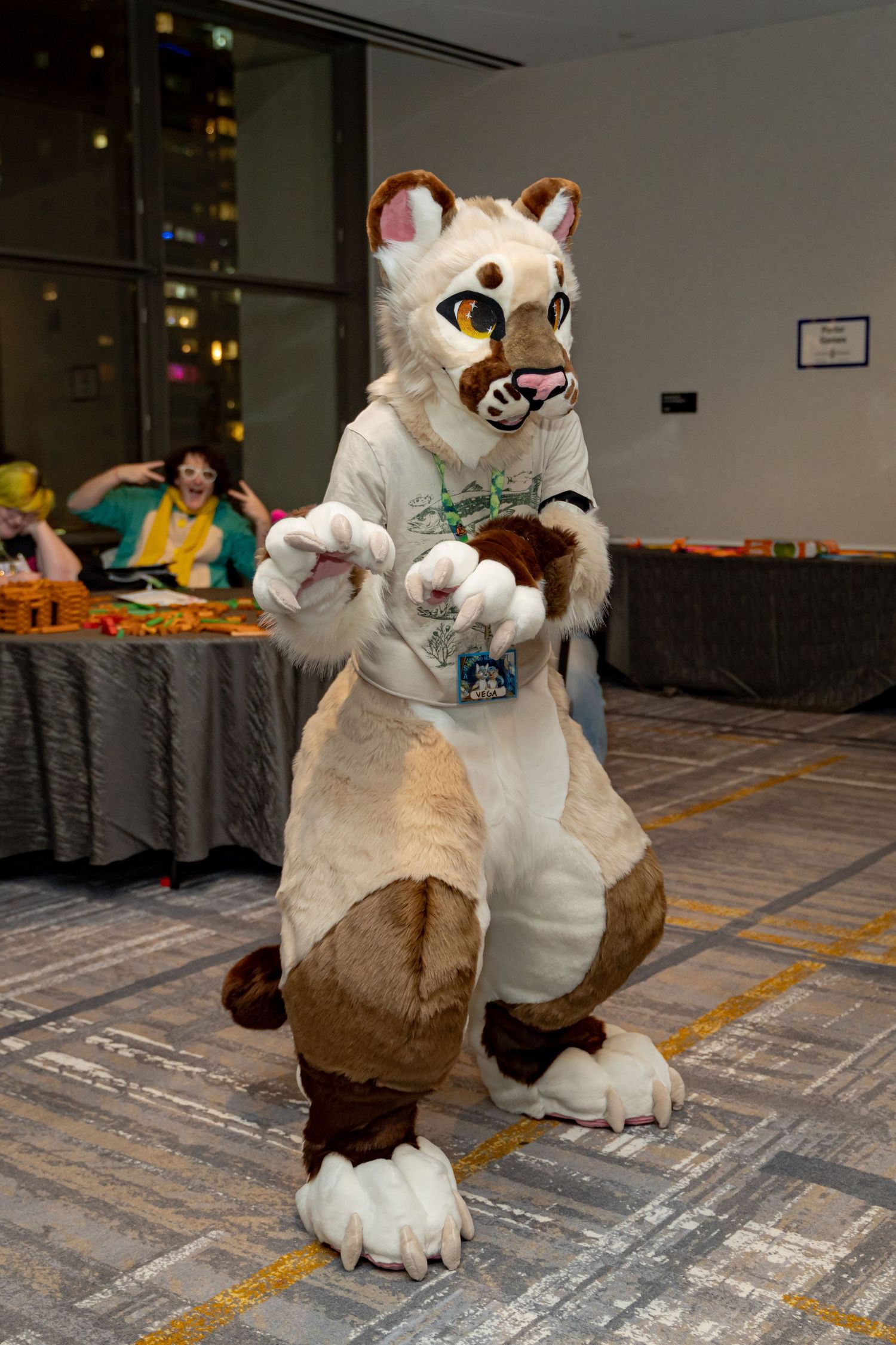 Two fursuit characters in white and brown costumes playfully interacting on a carpeted floor at a convention.