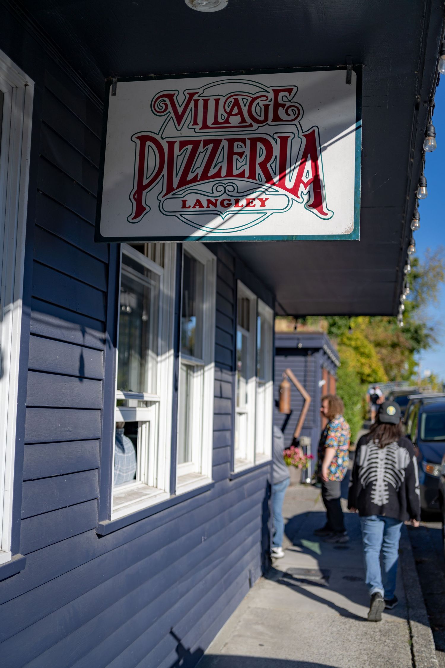 Exterior view of Village Pizzeria storefront with blue siding and signage.