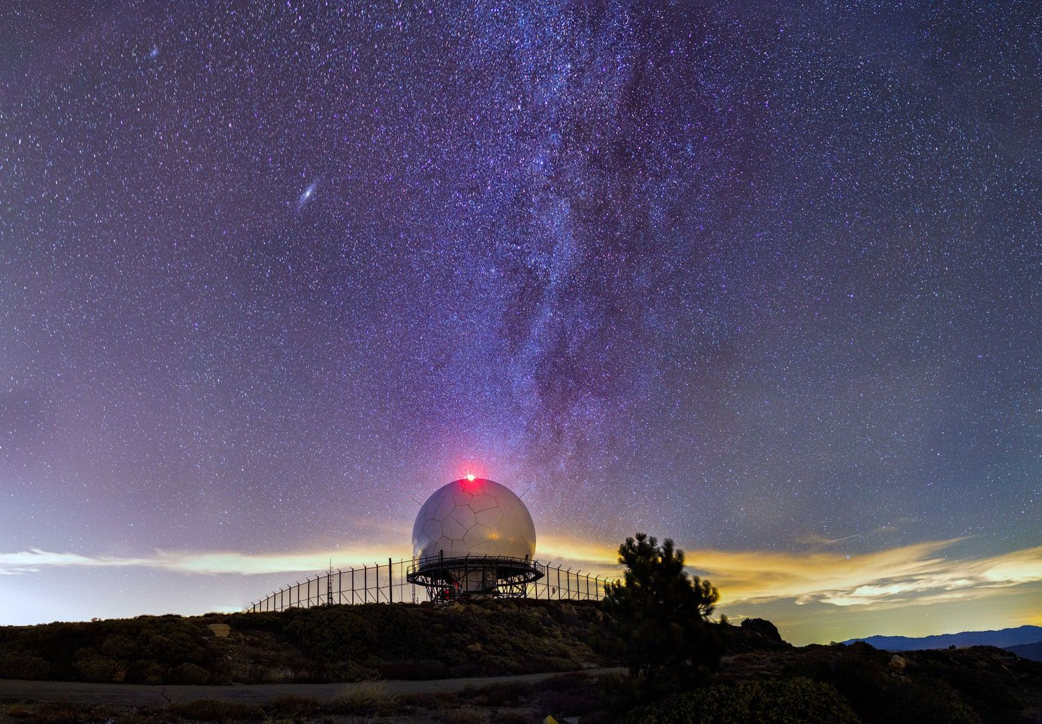 Night sky panorama showing the Milky Way galaxy stretching across a silhouetted horizon.