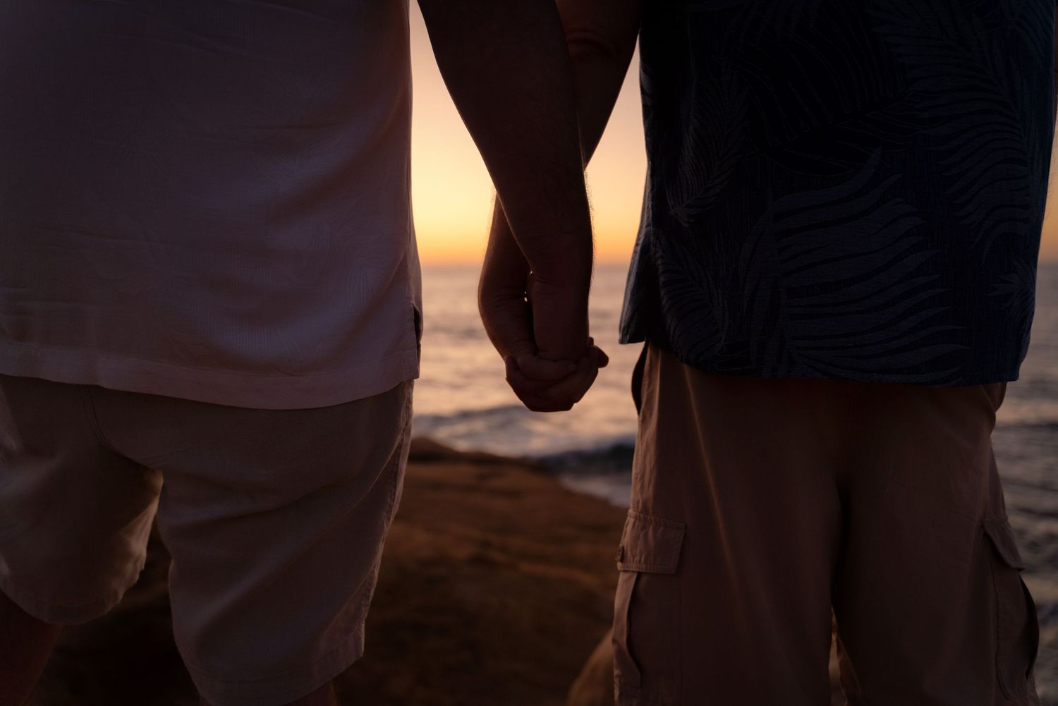 Close up of two people holding hands at sunset on a beach.