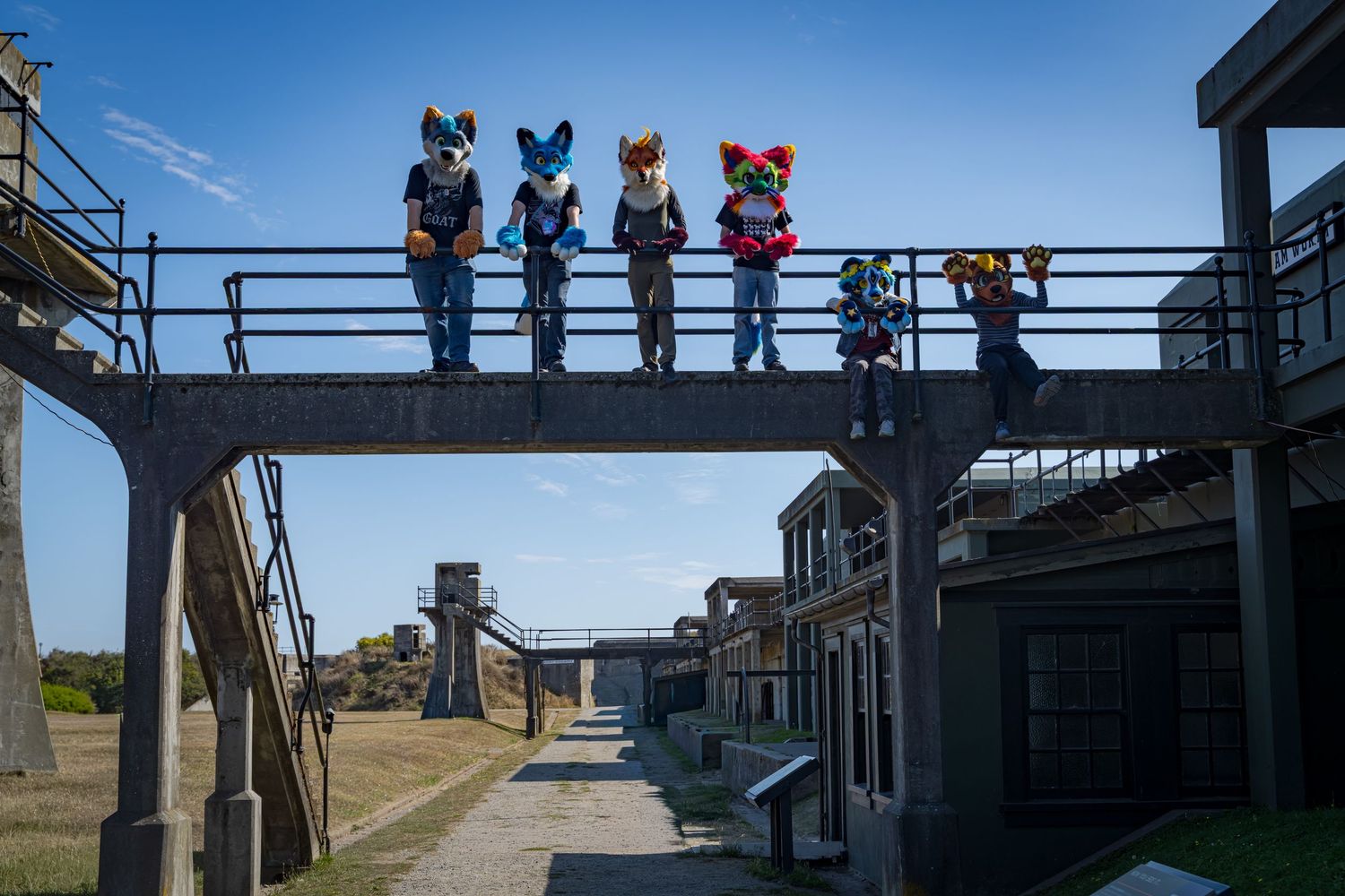 Group of fursuiters posing on elevated metal structure against blue sky.