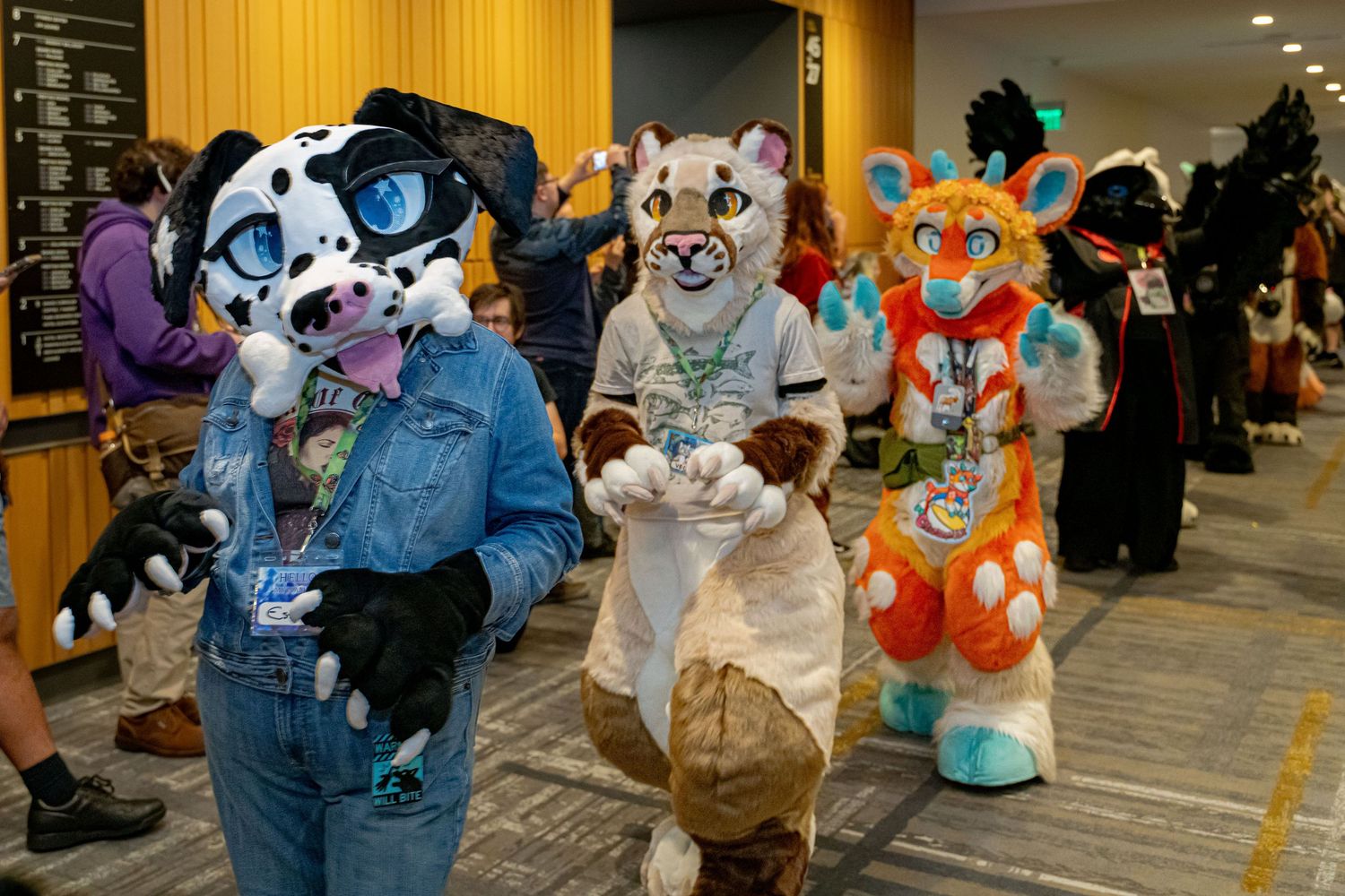 Fursuit enthusiasts in colorful animal costumes including a panda, wolf and tiger pose together at an indoor convention.