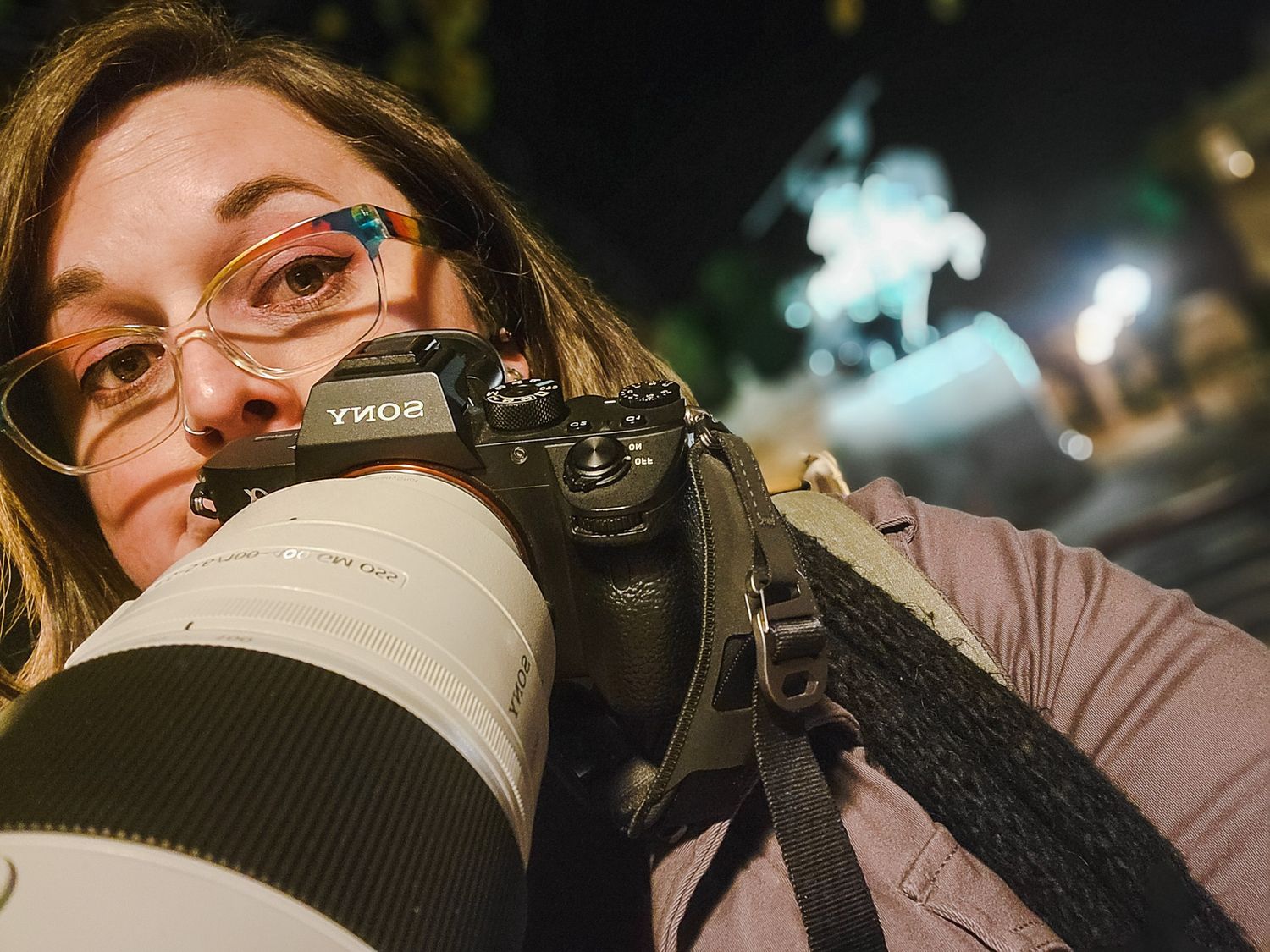 Camera enthusiast with glasses using photographic equipment in low light conditions.