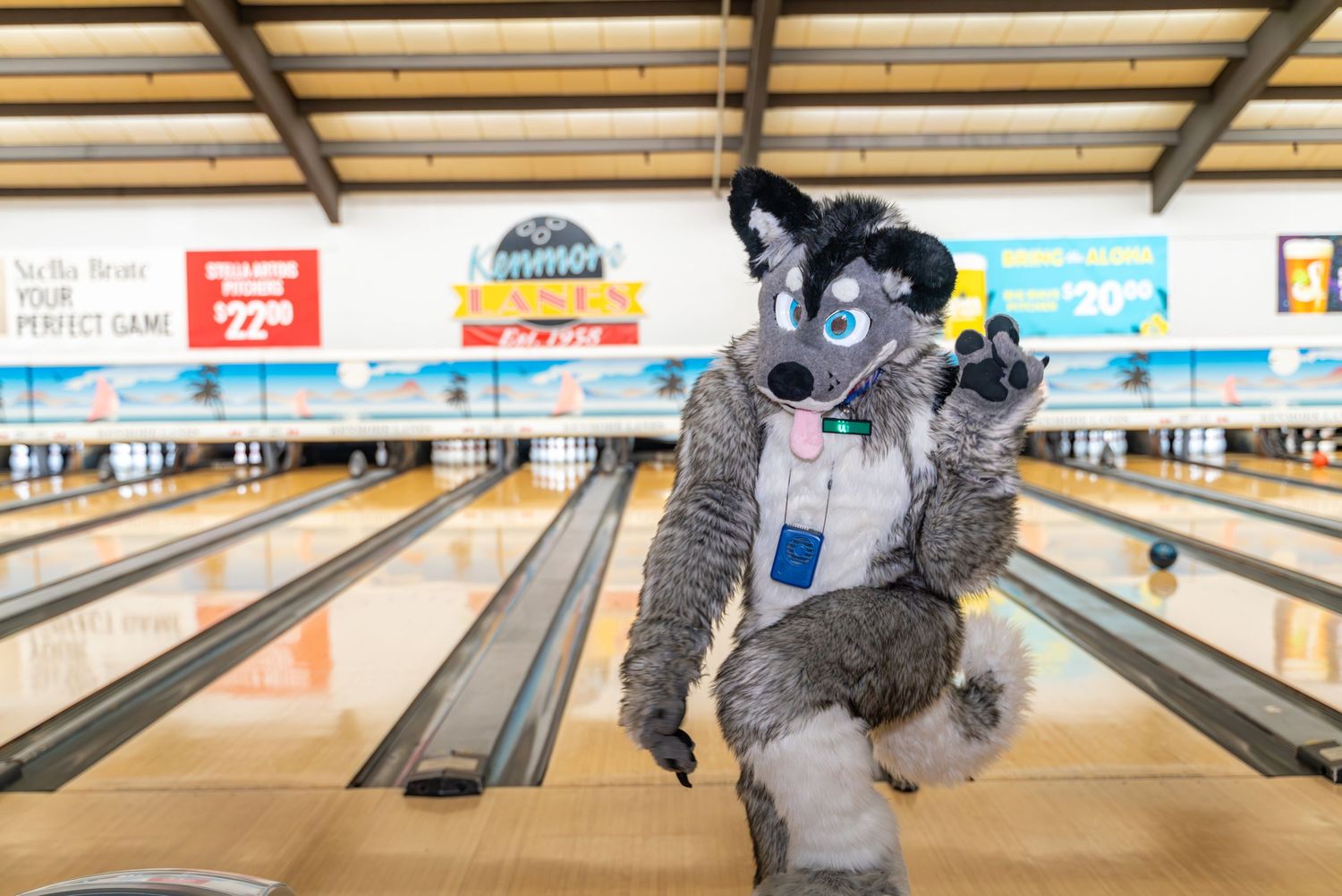 An enthusiastic fursuit character gestures while standing at the bowling lanes.
