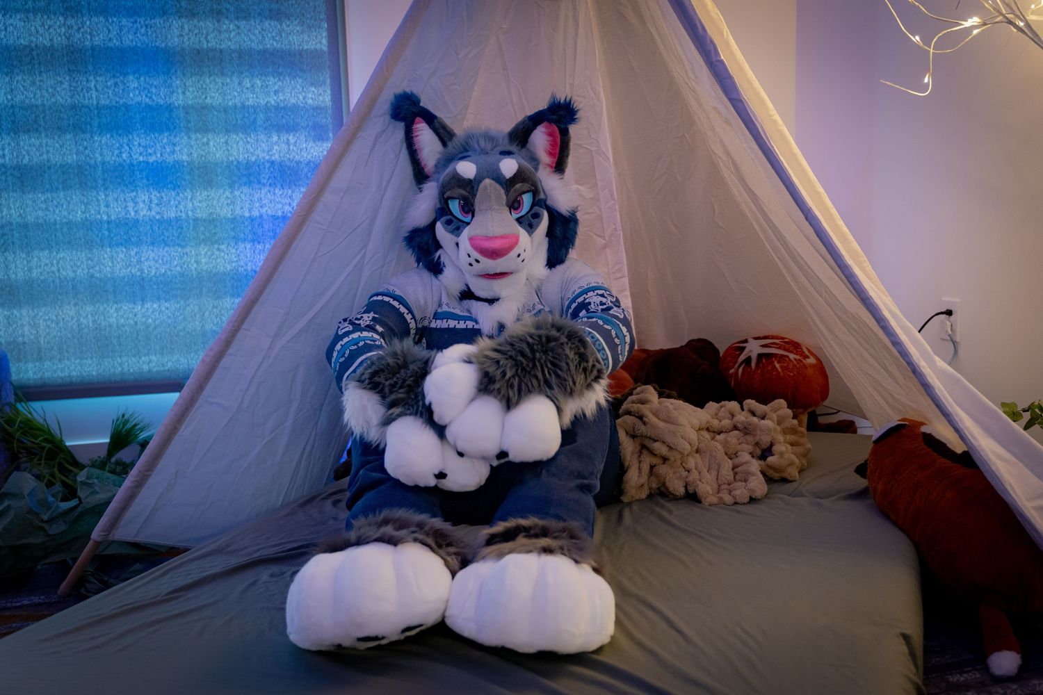 A plush furry character sits inside a tent setup with blue lighting and cozy bedding.