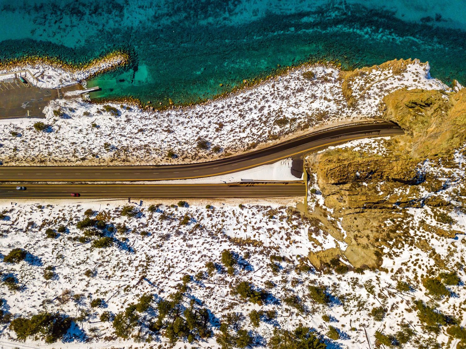 Panoramic winter coastline with snow-covered beach and dense forest meeting turquoise waters.
