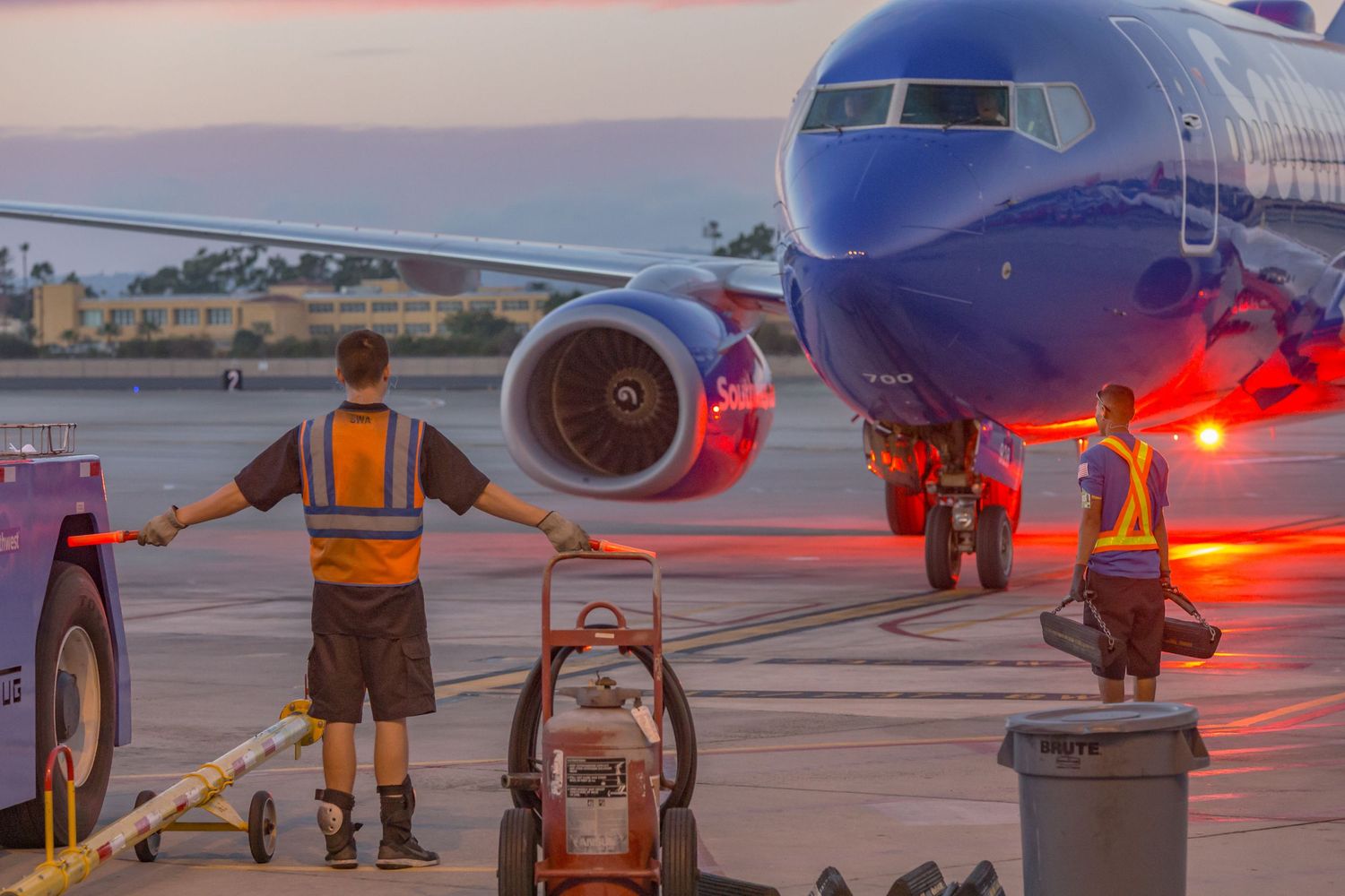 Ground crew servicing aircraft on tarmac during sunset with orange ambient lighting.