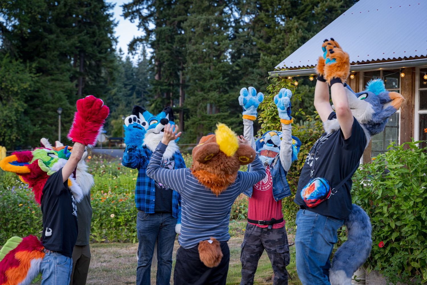 A group of people in bright costumes gather outdoors near farm buildings.