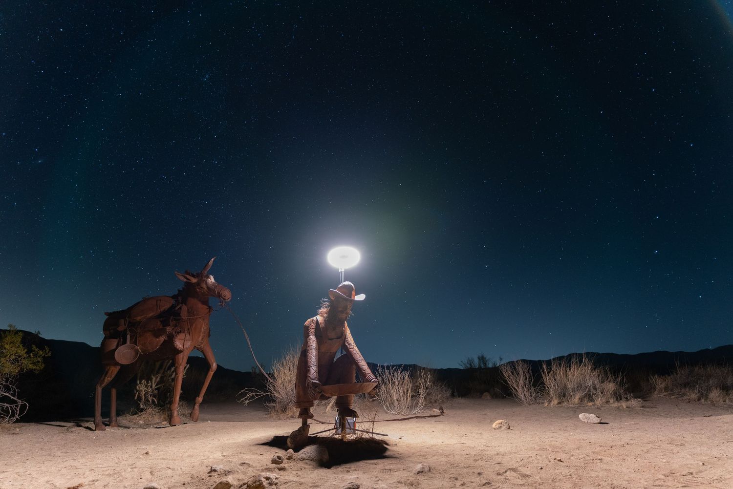 Desert landscape under a dark night sky with bright moonlight illuminating the terrain.