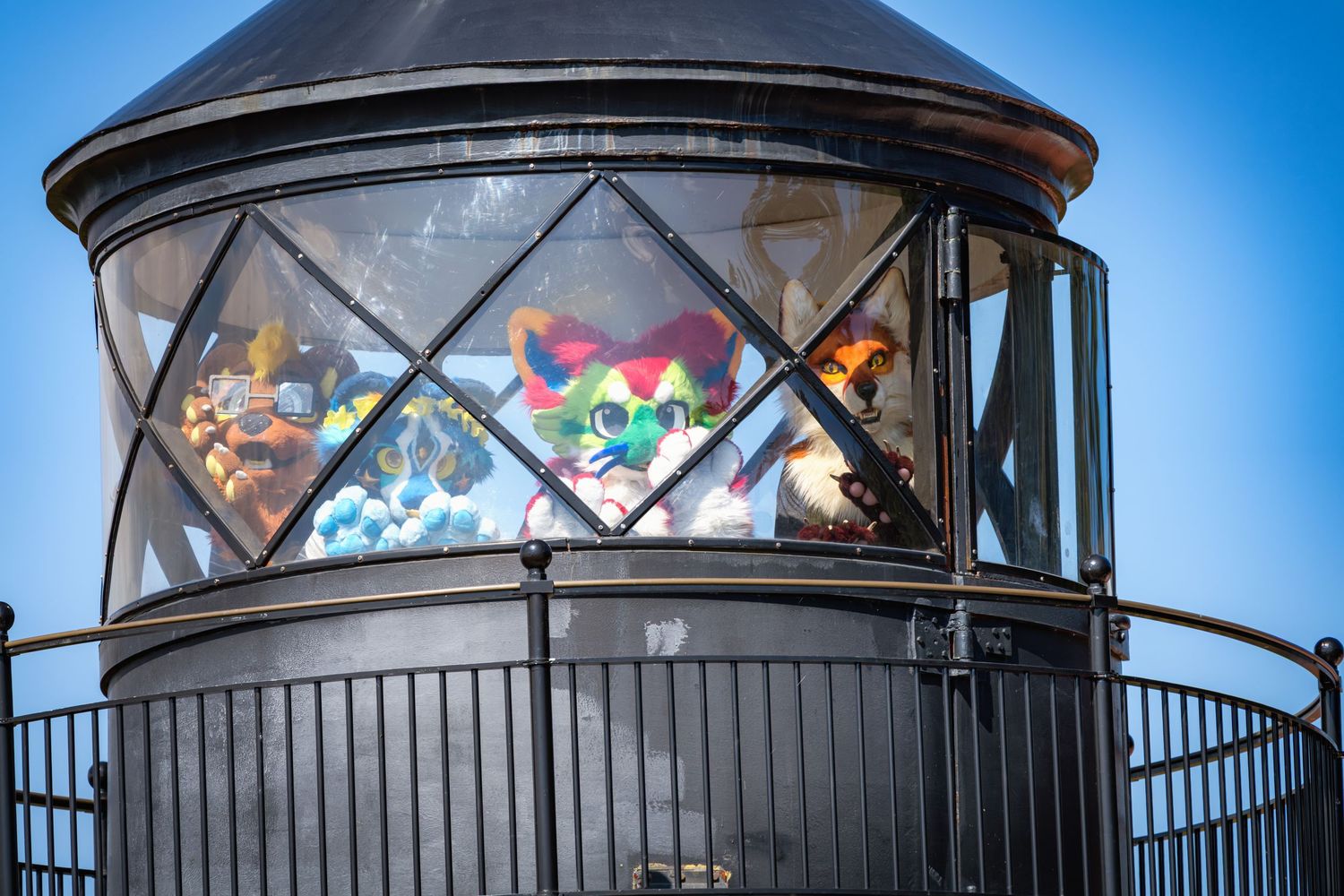 Black-domed lighthouse tower with decorative stained glass windows against bright blue sky.
