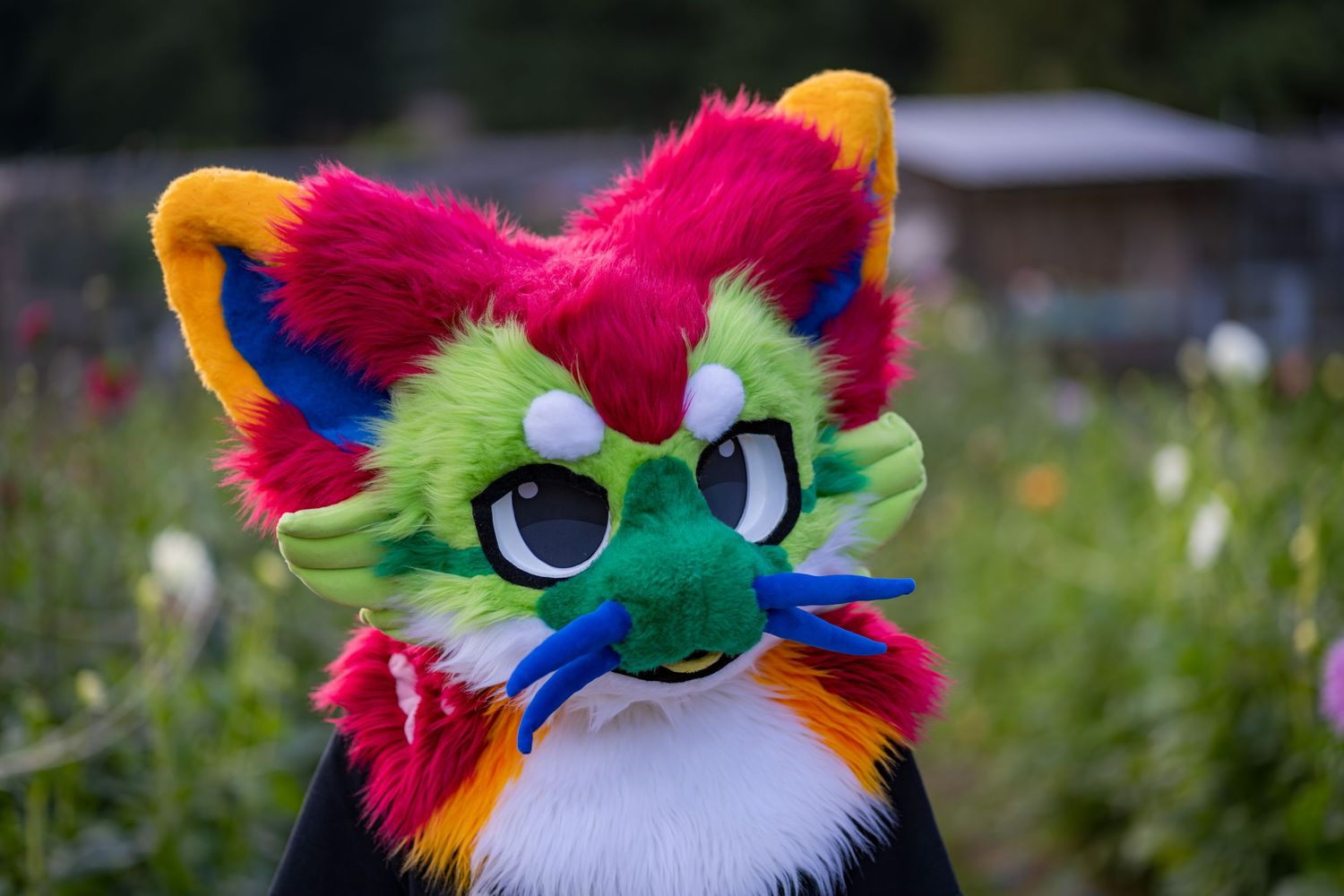 Colorful fursuit character with vibrant rainbow fur and expressive features poses in garden setting.