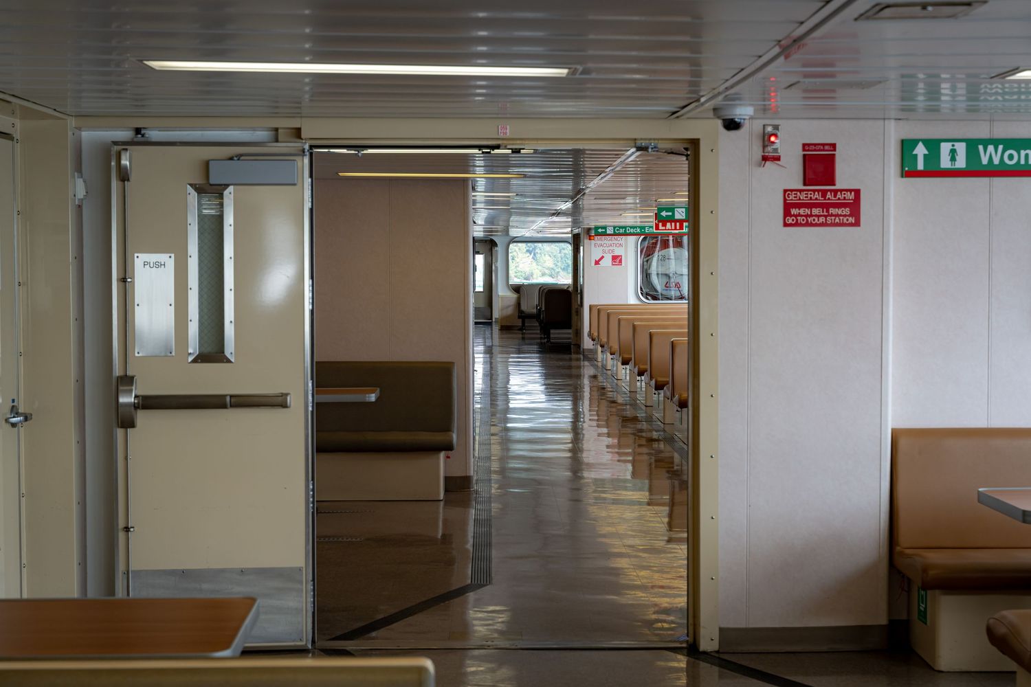 Long empty corridor inside a ferry with fluorescent lighting and emergency signs.