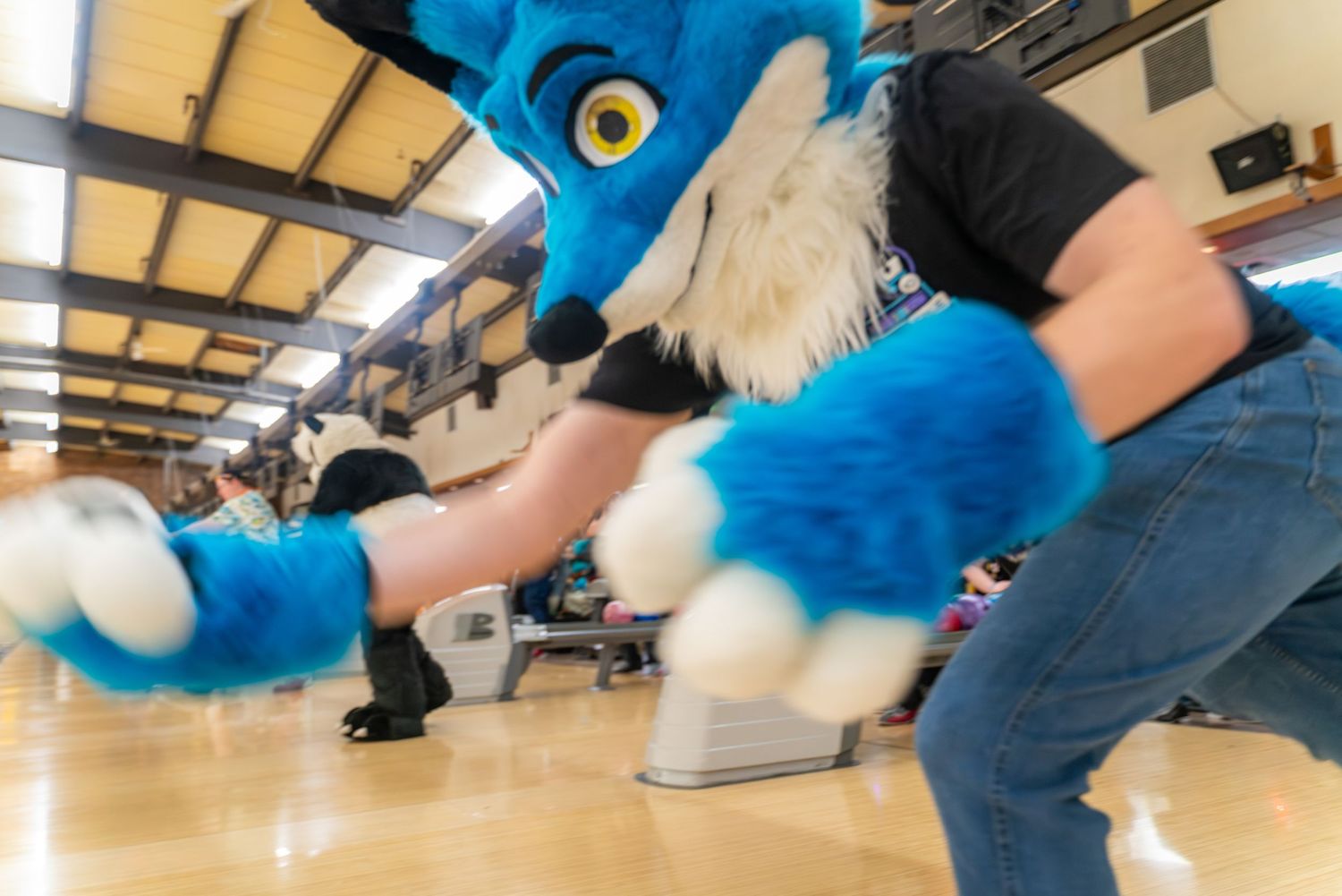 Blue fursuit characters pose low to the ground in a bowling alley setting.
