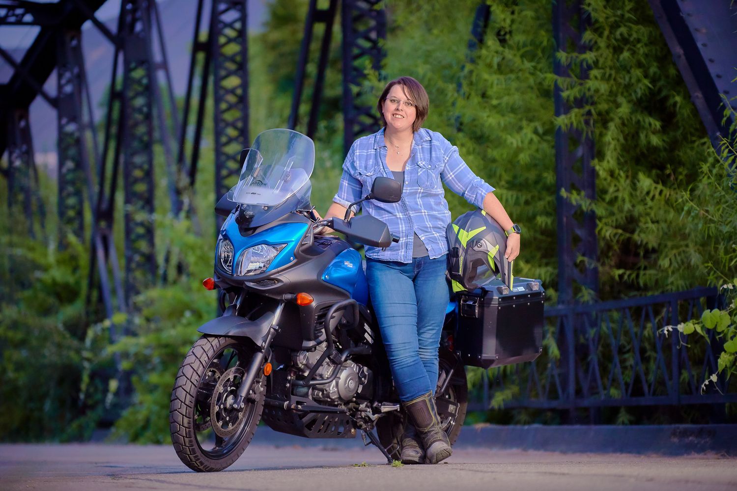 People relaxing near parked motorcycle on forest bridge during sunset.