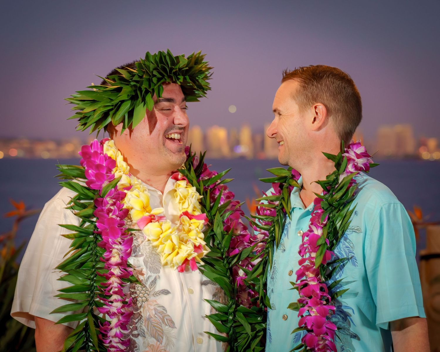 Couples wearing traditional Hawaiian leis against a twilight city backdrop.