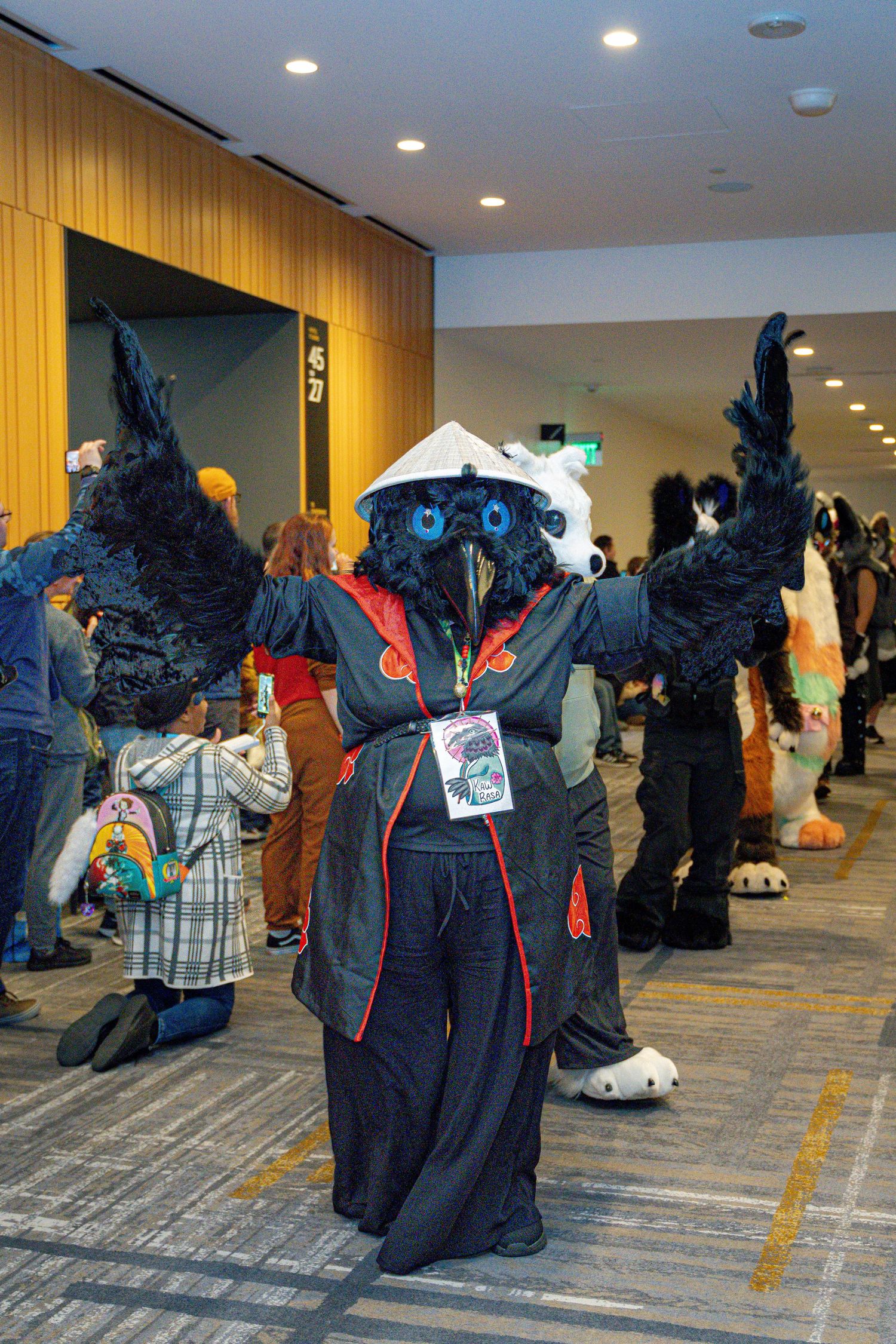 A line of people in black furry costumes with glowing blue eyes gather in a convention center hallway.