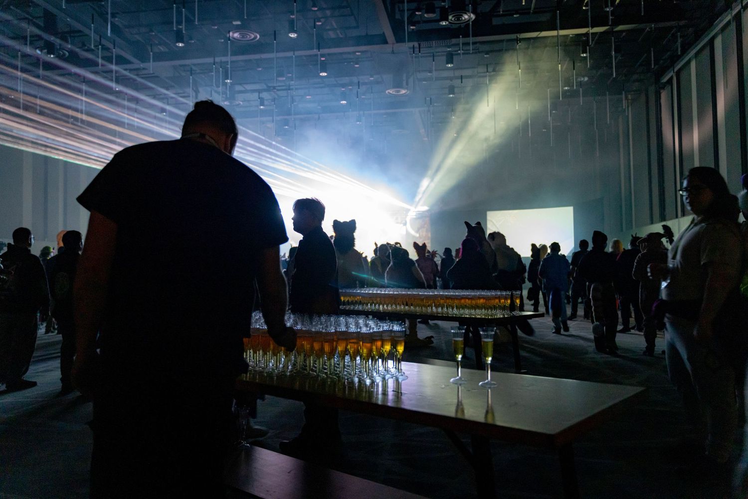A dark convention hall filled with silhouettes of attendees against bright backlighting.