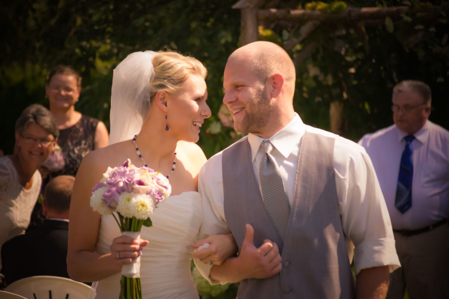 Wedding guests celebrate outdoors in a sunlit garden setting with festive atmosphere.