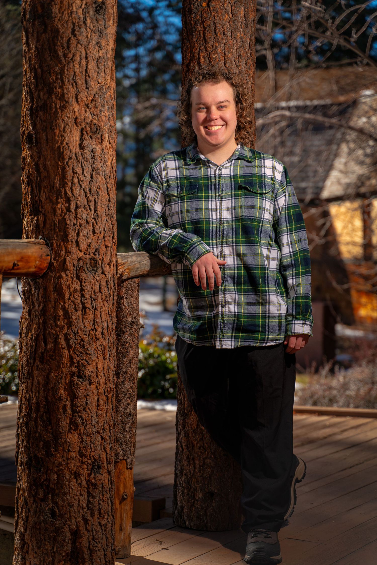 Portrait against pine trees showing someone wearing a green plaid shirt.
