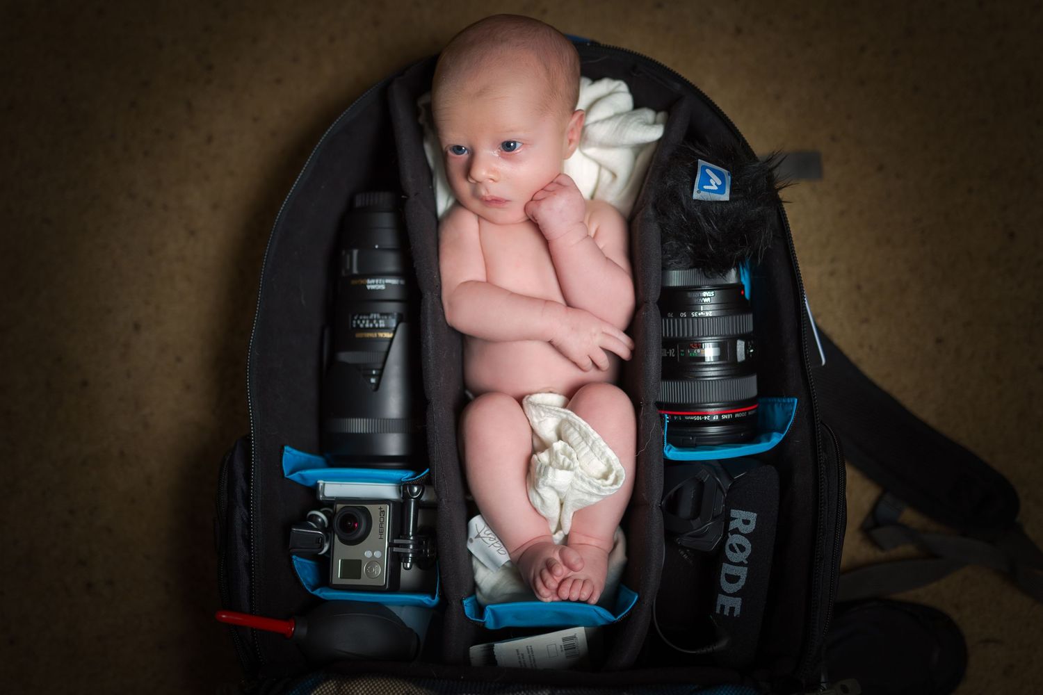 Creative newborn photography setup with baby posed among camera equipment.