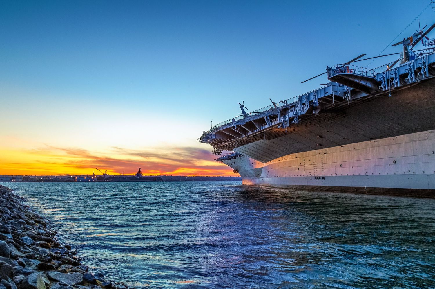 Dramatic ocean panorama at sunset showing waves crashing against a pier or structure.