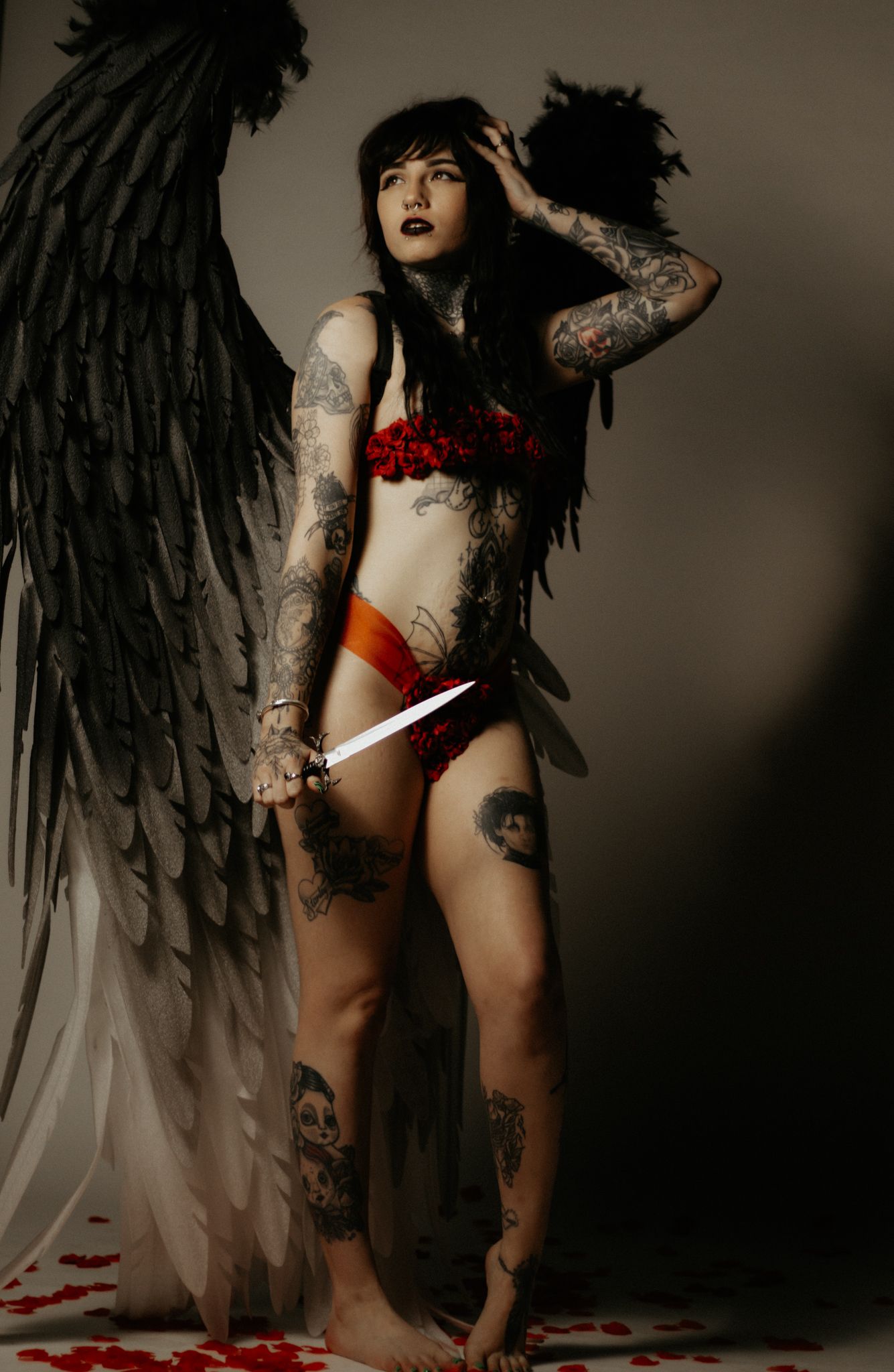 model poses with black wings wearing a red rose two piece lingerie set