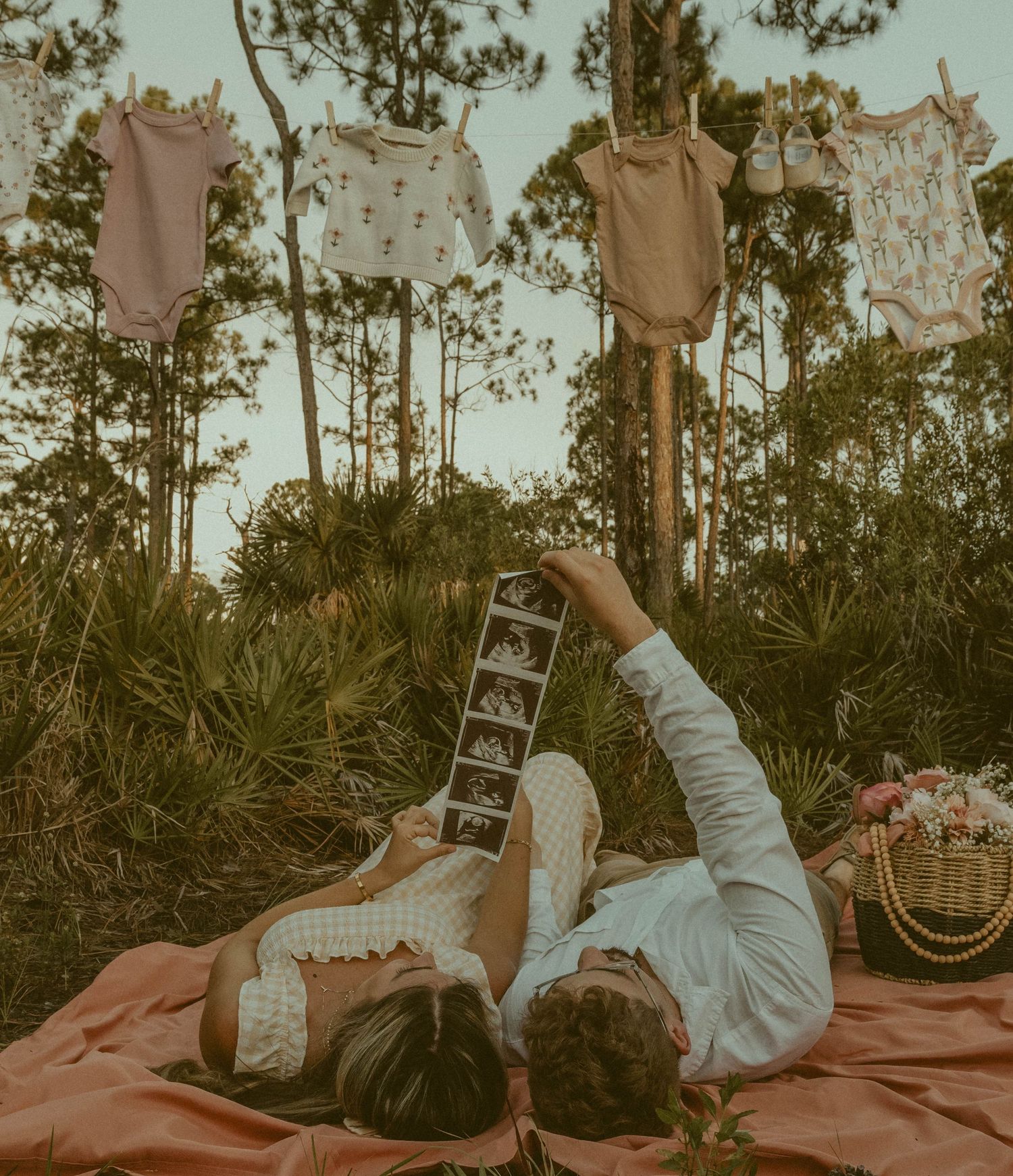 Couple lays on an orange sheet in myakka state park holding their sonogram of the new baby