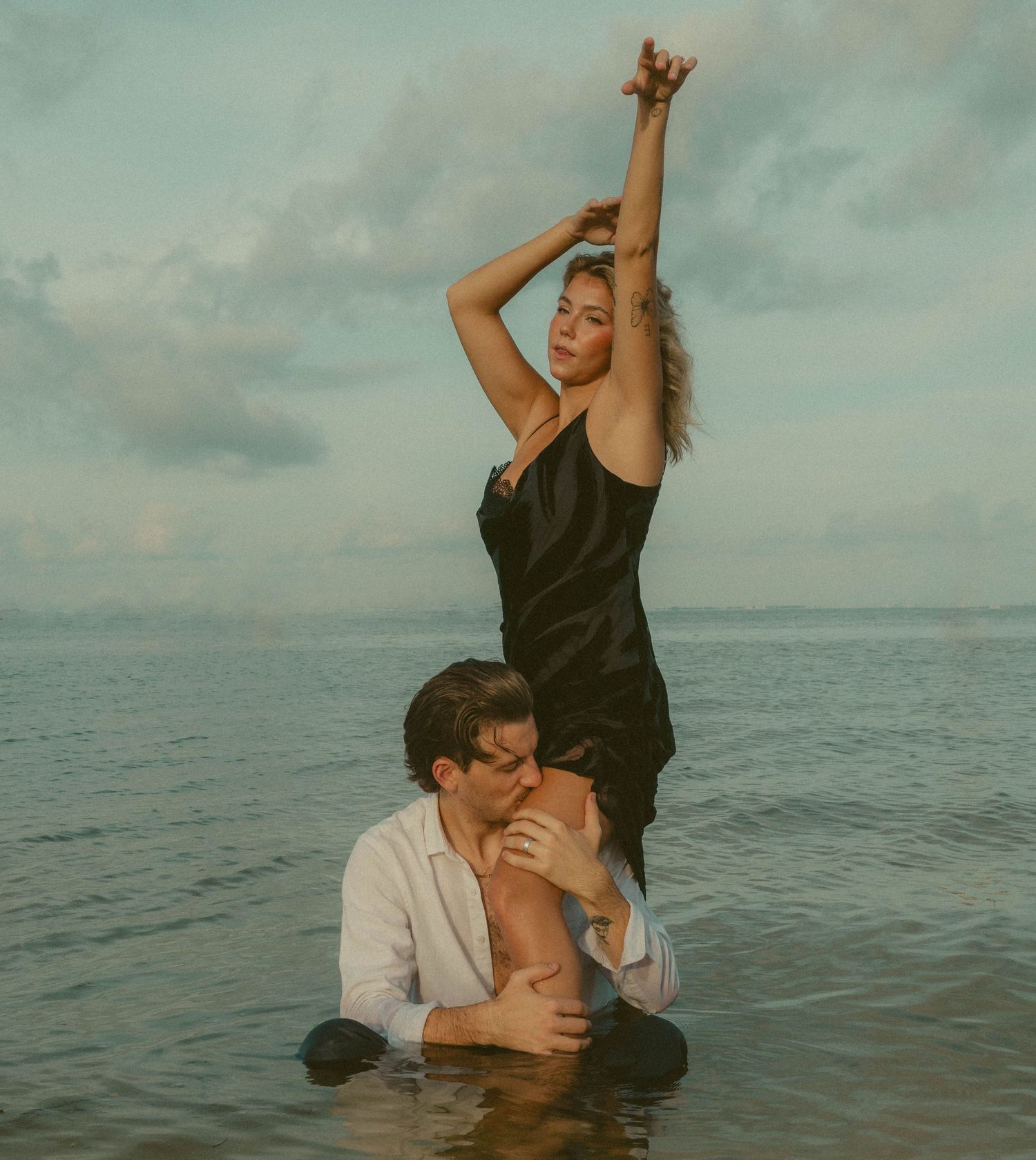 Couple poses in water near Tampa international airport. woman wears black dress and man wears gray tux