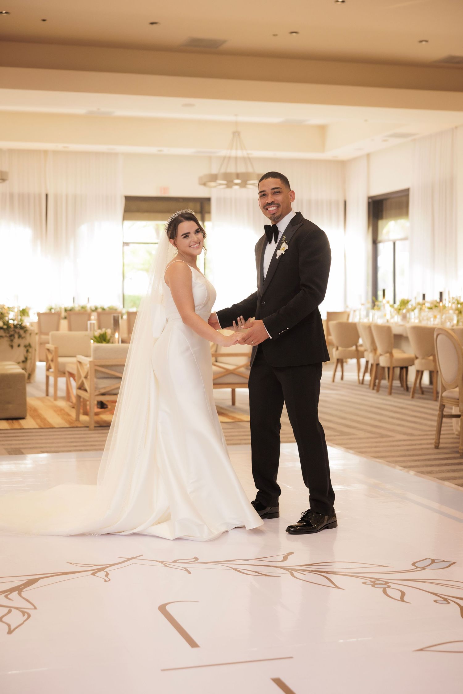 A smiling wedding couple shares a sweet moment on the white marble ballroom dance floor during their wedding reception.