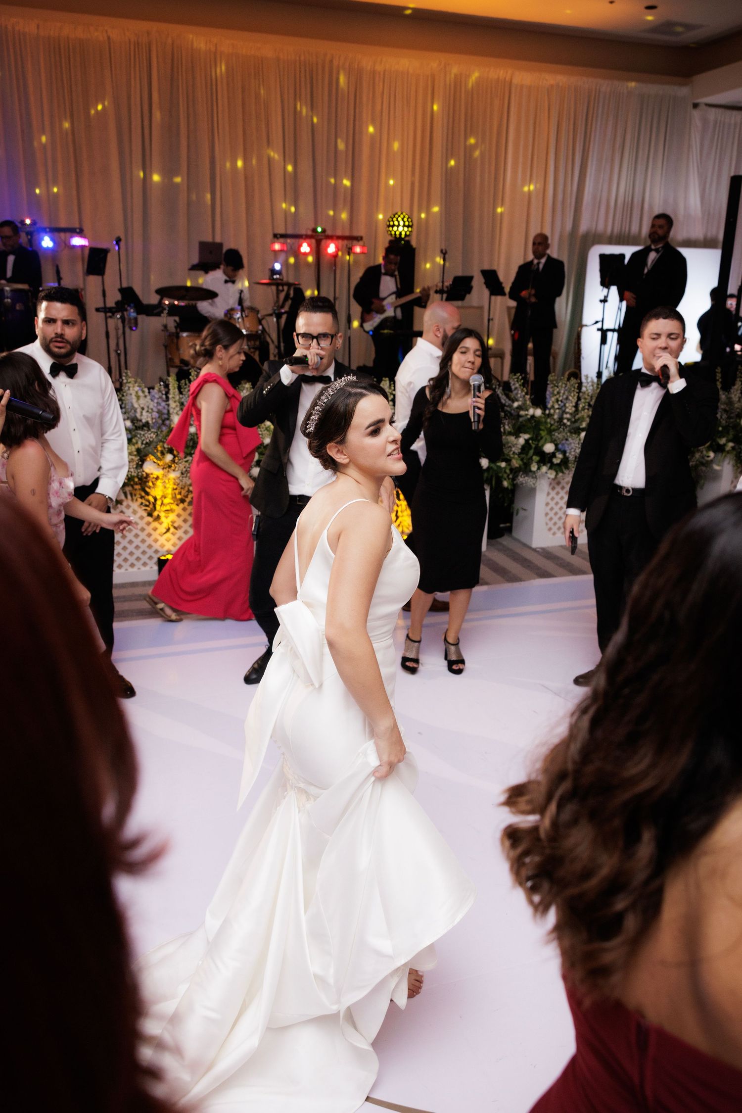 A joyful dance scene at an elegant wedding reception with white decor and twinkling lights in the background.