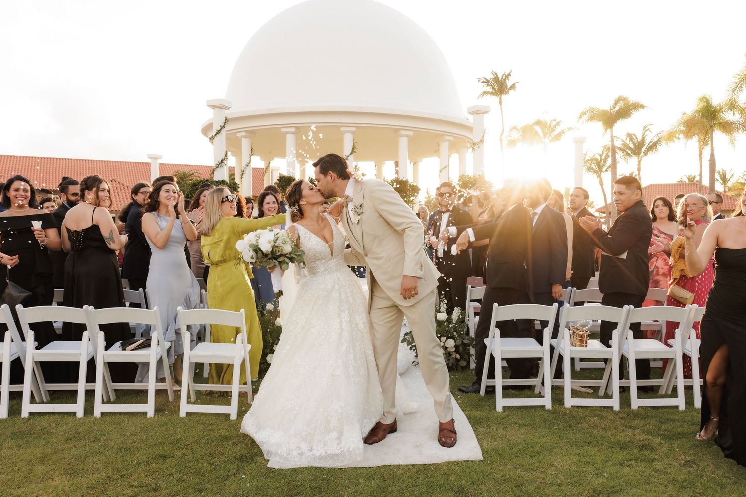 Wedding celebration at sunset creates stunning golden silhouettes against palm trees and ocean backdrop on outdoor terrace.