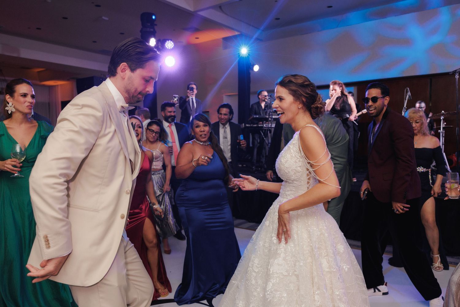 A couple dances together during a wedding reception with festive blue lighting and guests watching in the background.
