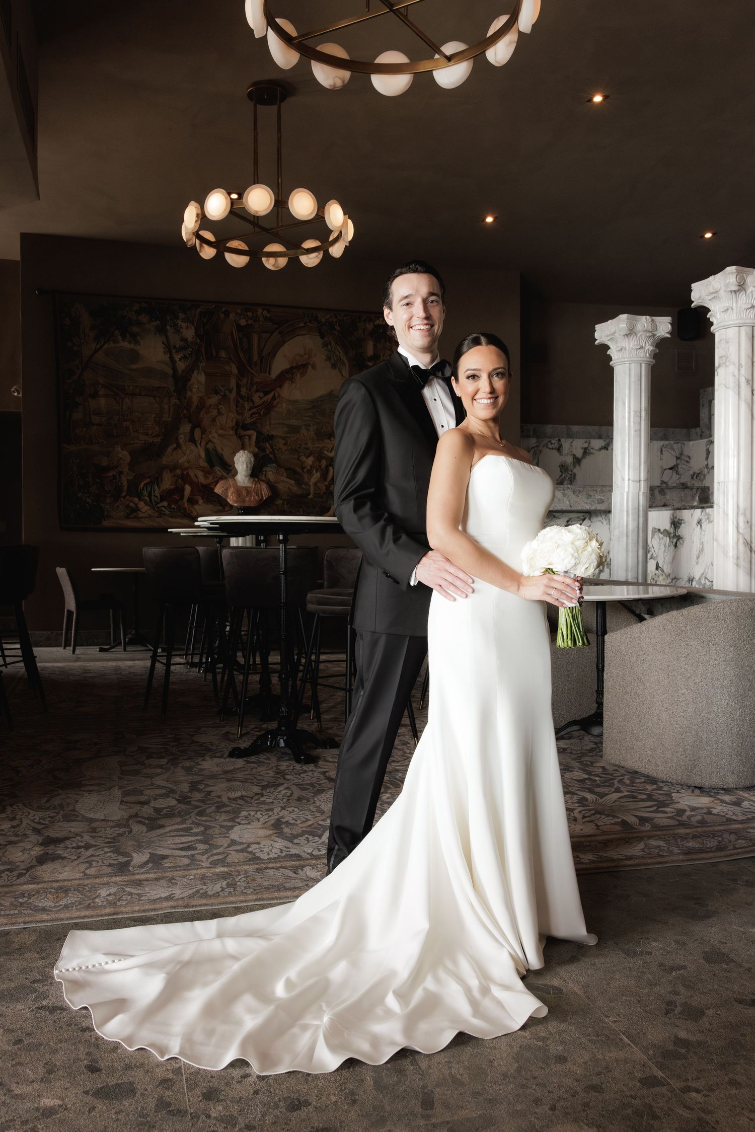 Couple dancing in an elegant venue with ornate lighting and white decor.