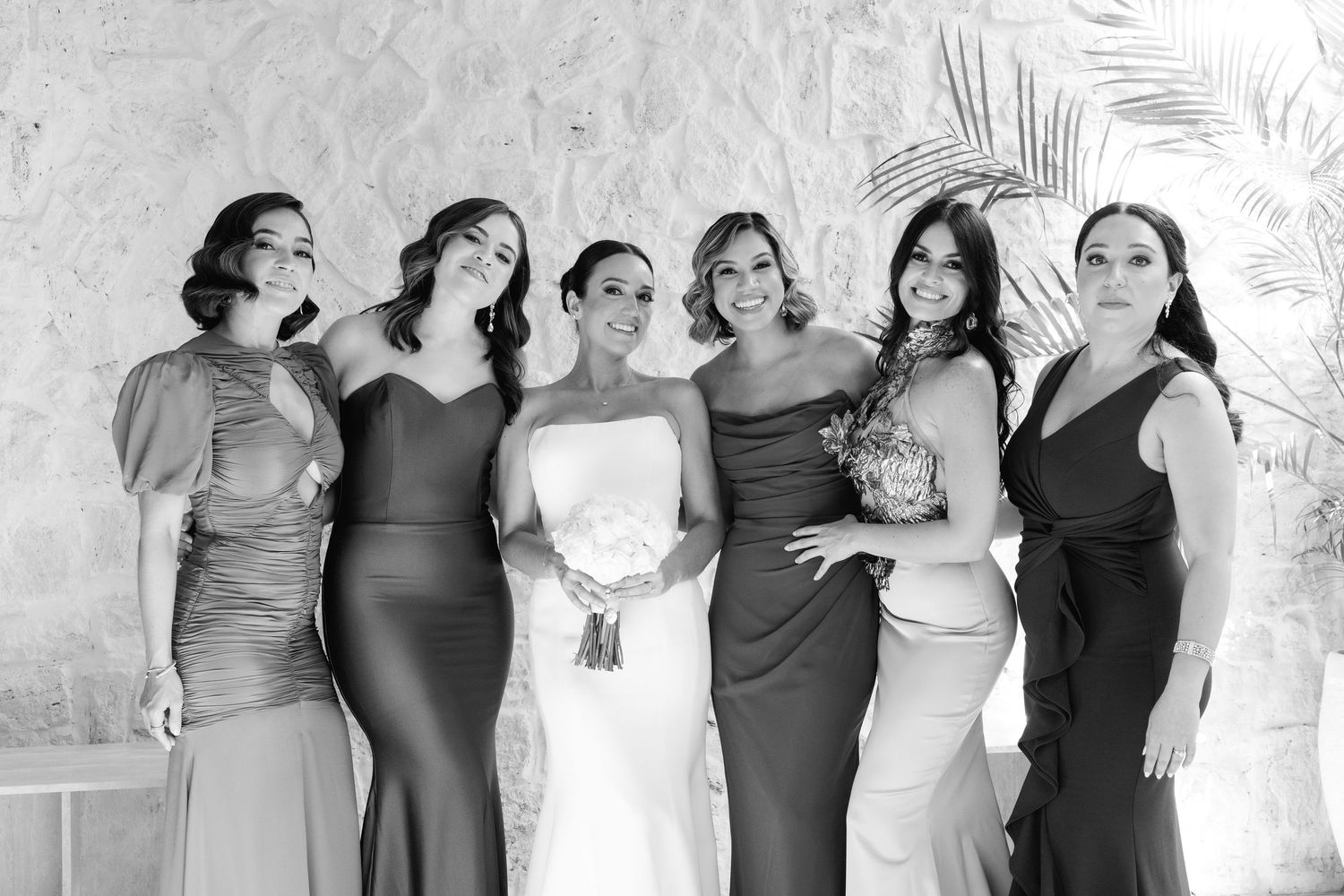 Line of bridesmaids in coordinating dark dresses standing together during a formal wedding event.
